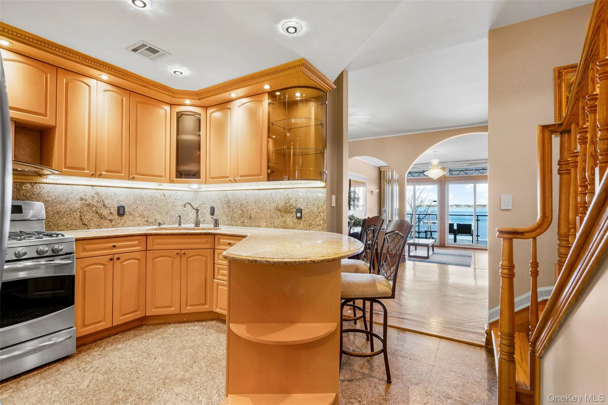 Kitchen featuring glass insert cabinets, open shelves, arched walkways, stainless steel gas range oven, and light stone counters Kitchen featuring glass insert cabinets, open shelves, arched walkways, stainless steel gas range oven, and light stone counters
