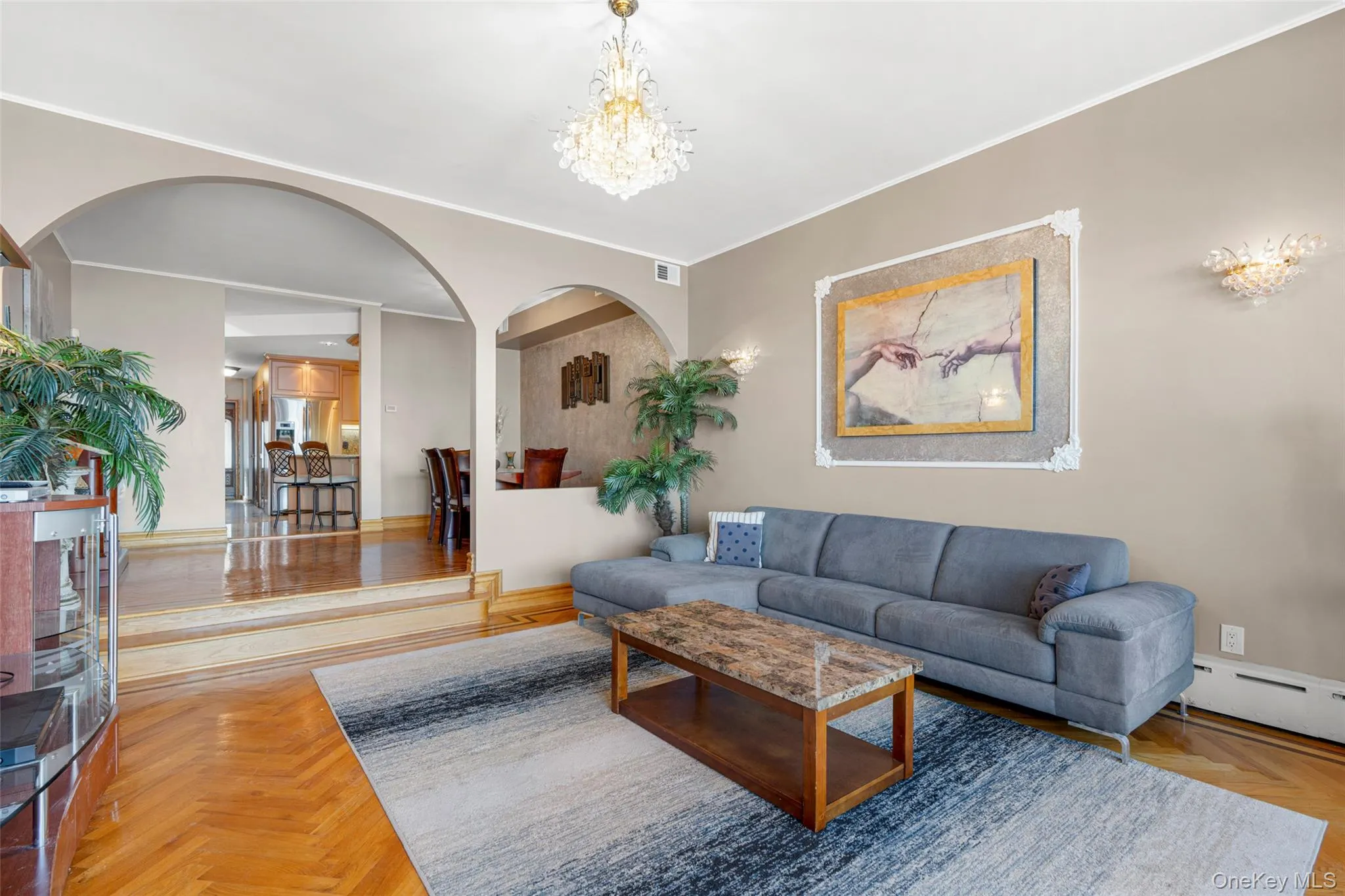 Living room featuring arched walkways, a chandelier, a baseboard radiator, and ornamental molding Living room featuring arched walkways, a chandelier, a baseboard radiator, and ornamental molding