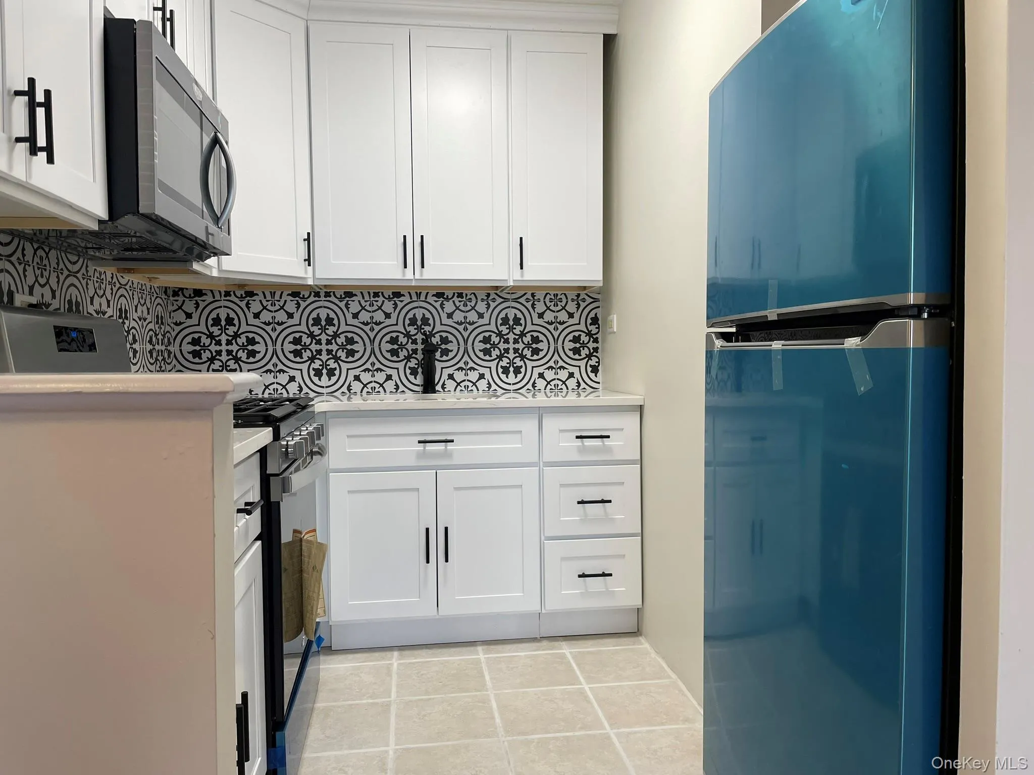 Kitchen with light countertops, white cabinetry, fridge, and decorative backsplash Kitchen with light countertops, white cabinetry, fridge, and decorative backsplash