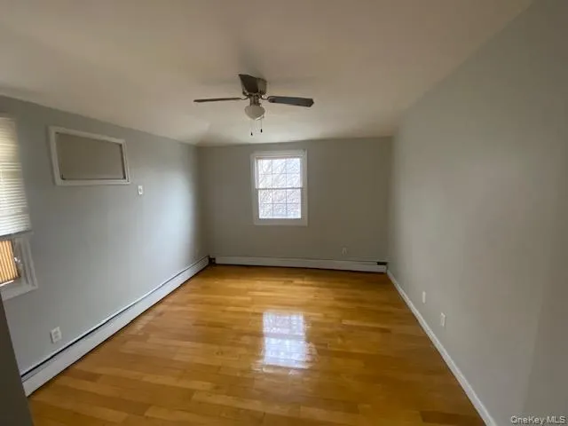 Empty room featuring baseboard heating, light wood-style flooring, a baseboard heating unit, and a ceiling fan Empty room featuring baseboard heating, light wood-style flooring, a baseboard heating unit, and a ceiling fan