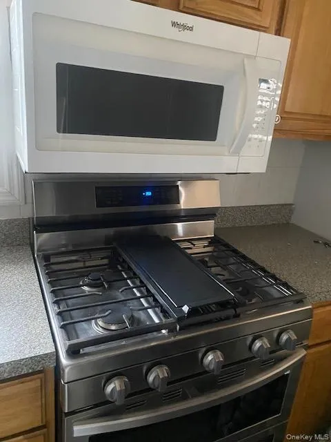 Kitchen view of white microwave, brown cabinetry, dark countertops, and stainless steel gas range oven Kitchen view of white microwave, brown cabinetry, dark countertops, and stainless steel gas range oven