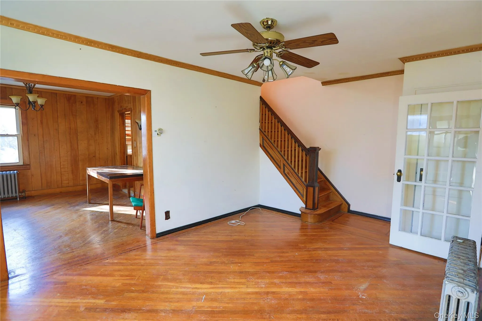 Unfurnished living room featuring wood-type flooring, radiator heating unit, crown molding, stairs, and a chandelier Unfurnished living room featuring wood-type flooring, radiator heating unit, crown molding, stairs, and a chandelier