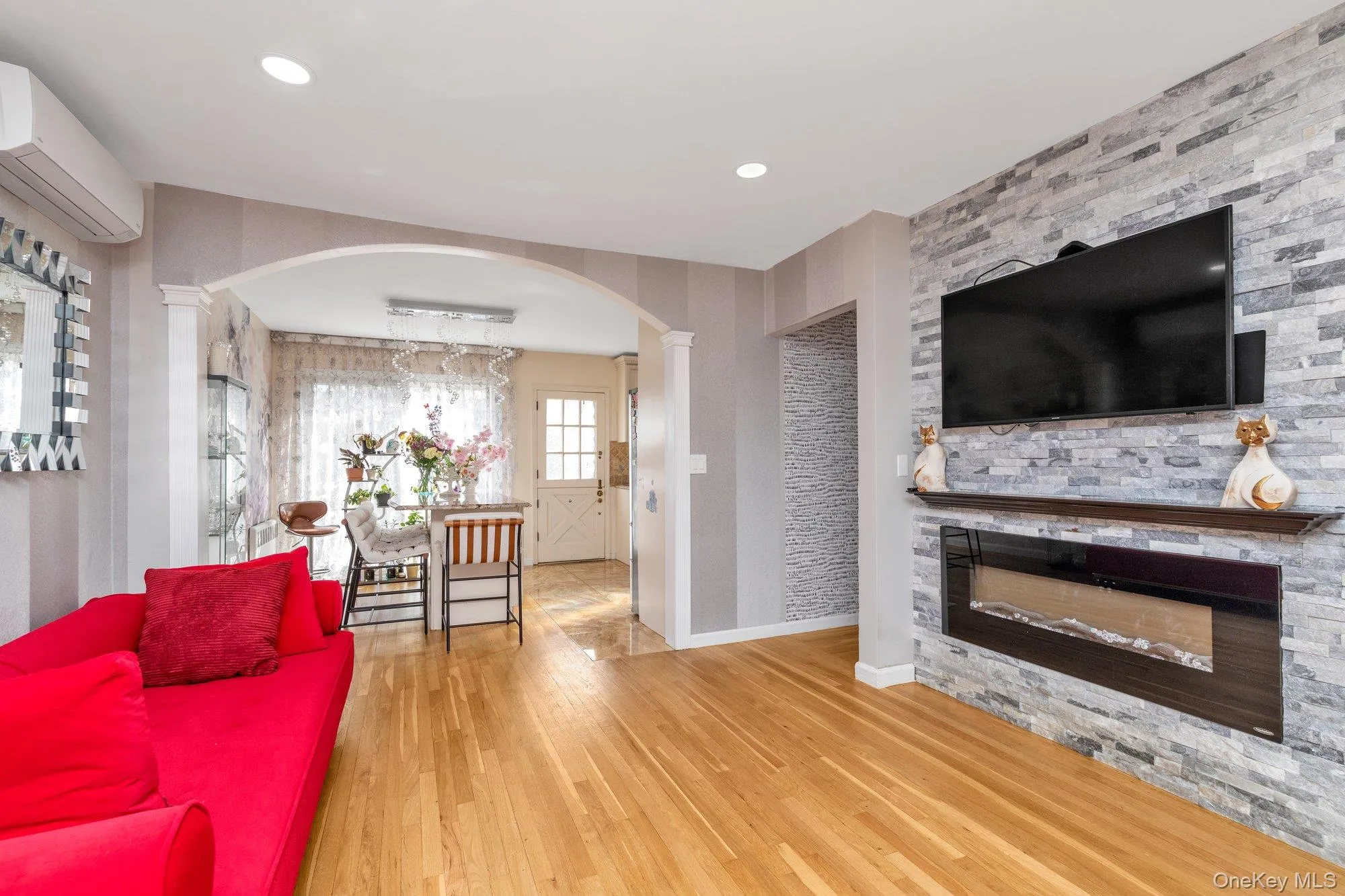 Living room with arched walkways, a glass covered fireplace, wood finished floors, a wall mounted air conditioner, and recessed lighting Living room with arched walkways, a glass covered fireplace, wood finished floors, a wall mounted air conditioner, and recessed lighting