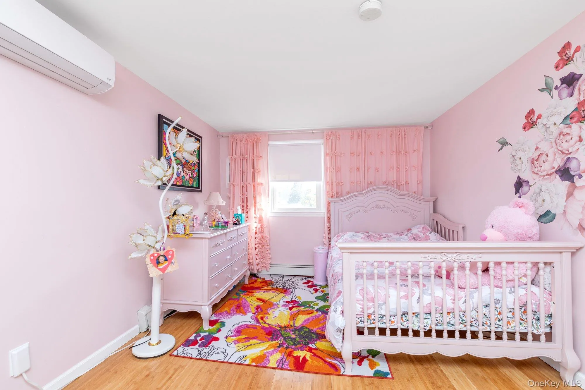 Bedroom featuring a wall mounted AC, light wood finished floors, a crib, and a baseboard radiator Bedroom featuring a wall mounted AC, light wood finished floors, a crib, and a baseboard radiator