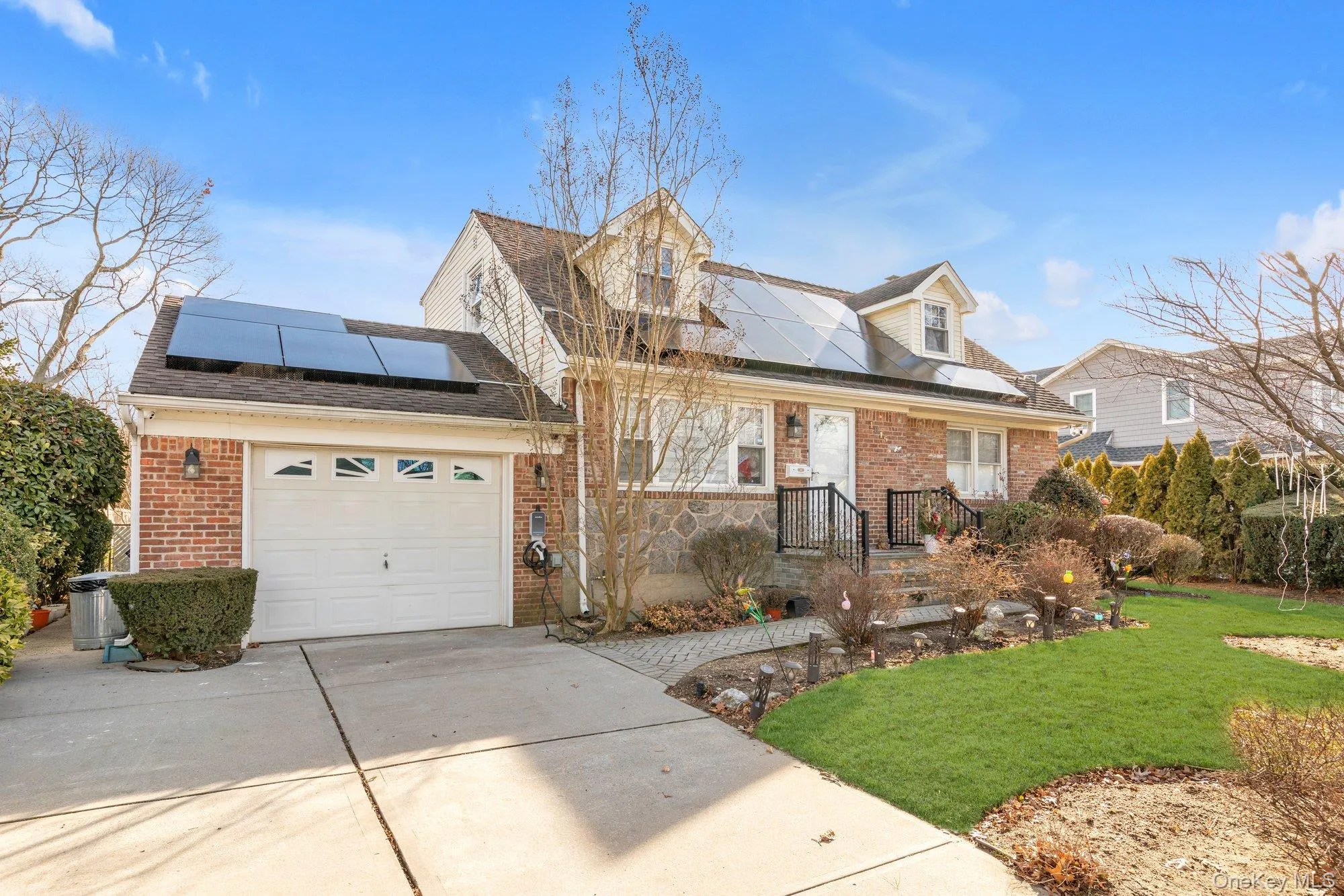 View of front of home with brick siding, a front lawn, driveway, and roof mounted solar panels View of front of home with brick siding, a front lawn, driveway, and roof mounted solar panels