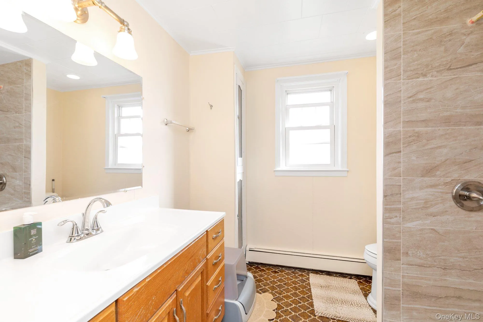 Bathroom featuring a baseboard radiator, vanity, a tile shower, plenty of natural light, and ornamental molding Bathroom featuring a baseboard radiator, vanity, a tile shower, plenty of natural light, and ornamental molding