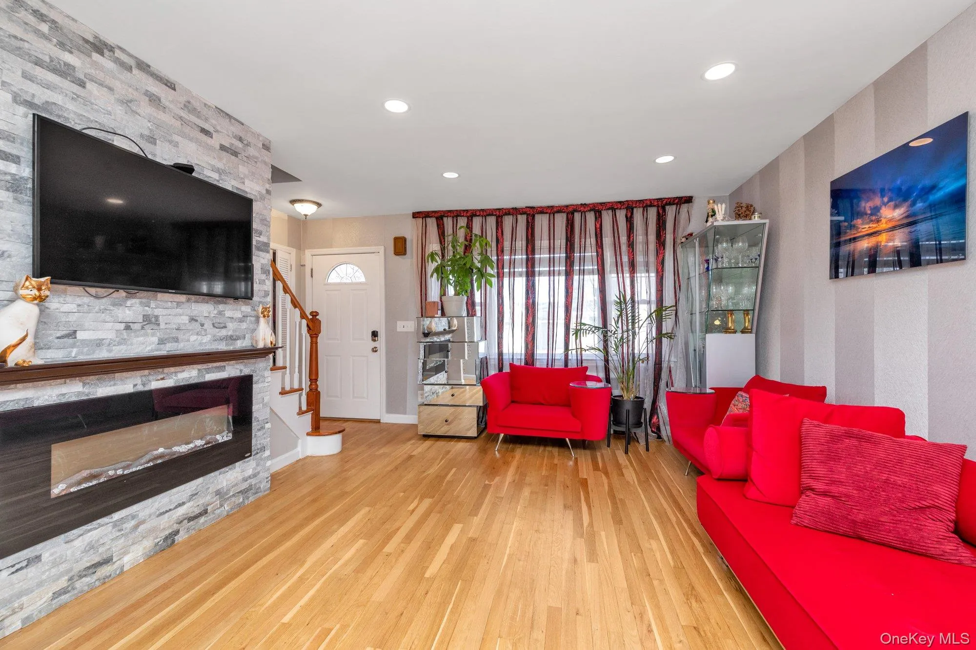 Living area featuring stairway, wood finished floors, recessed lighting, a glass covered fireplace, and wallpapered walls Living area featuring stairway, wood finished floors, recessed lighting, a glass covered fireplace, and wallpapered walls