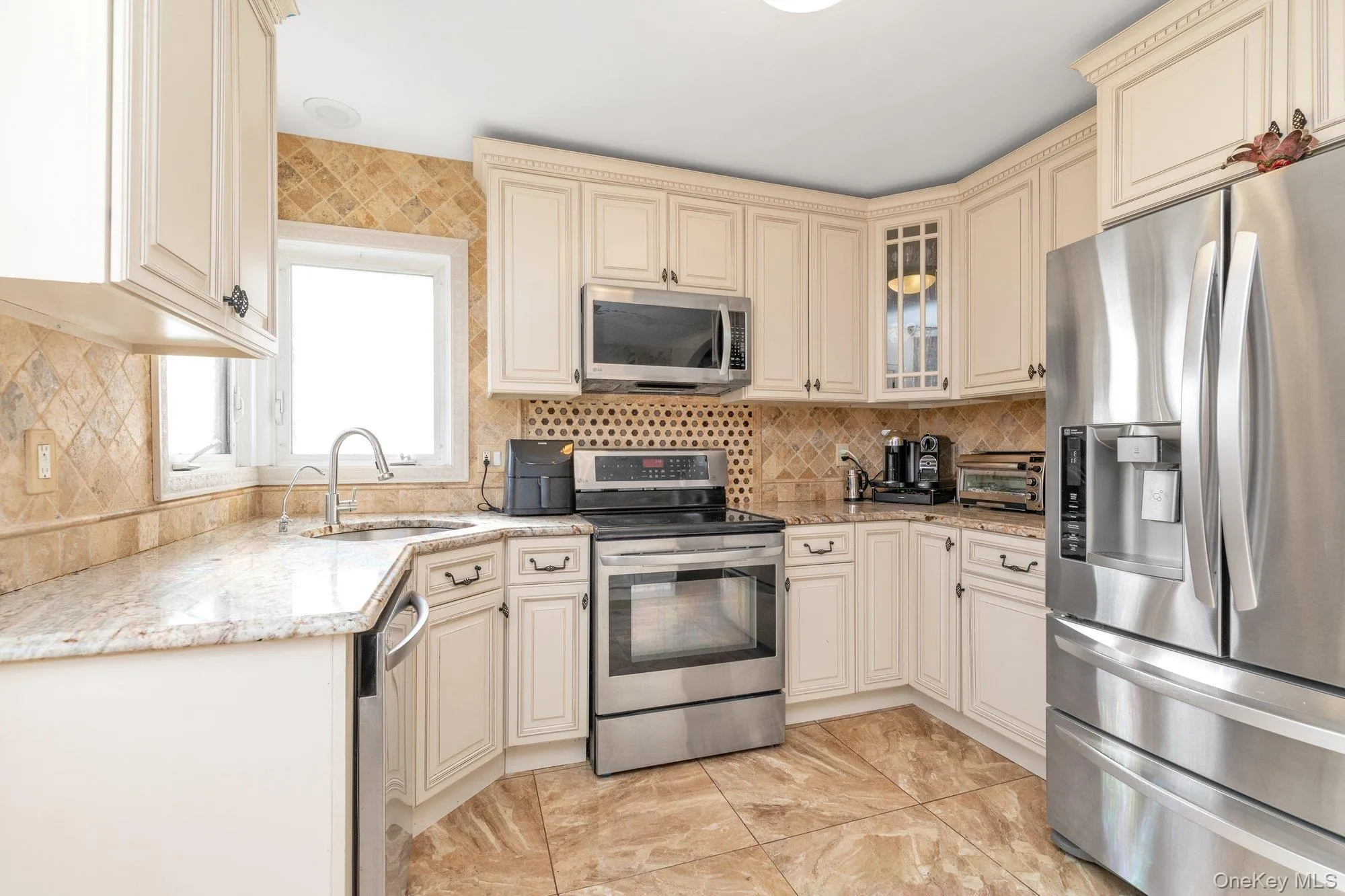 Kitchen with cream cabinets, stainless steel appliances, light stone countertops, decorative backsplash, and glass insert cabinets Kitchen with cream cabinets, stainless steel appliances, light stone countertops, decorative backsplash, and glass insert cabinets