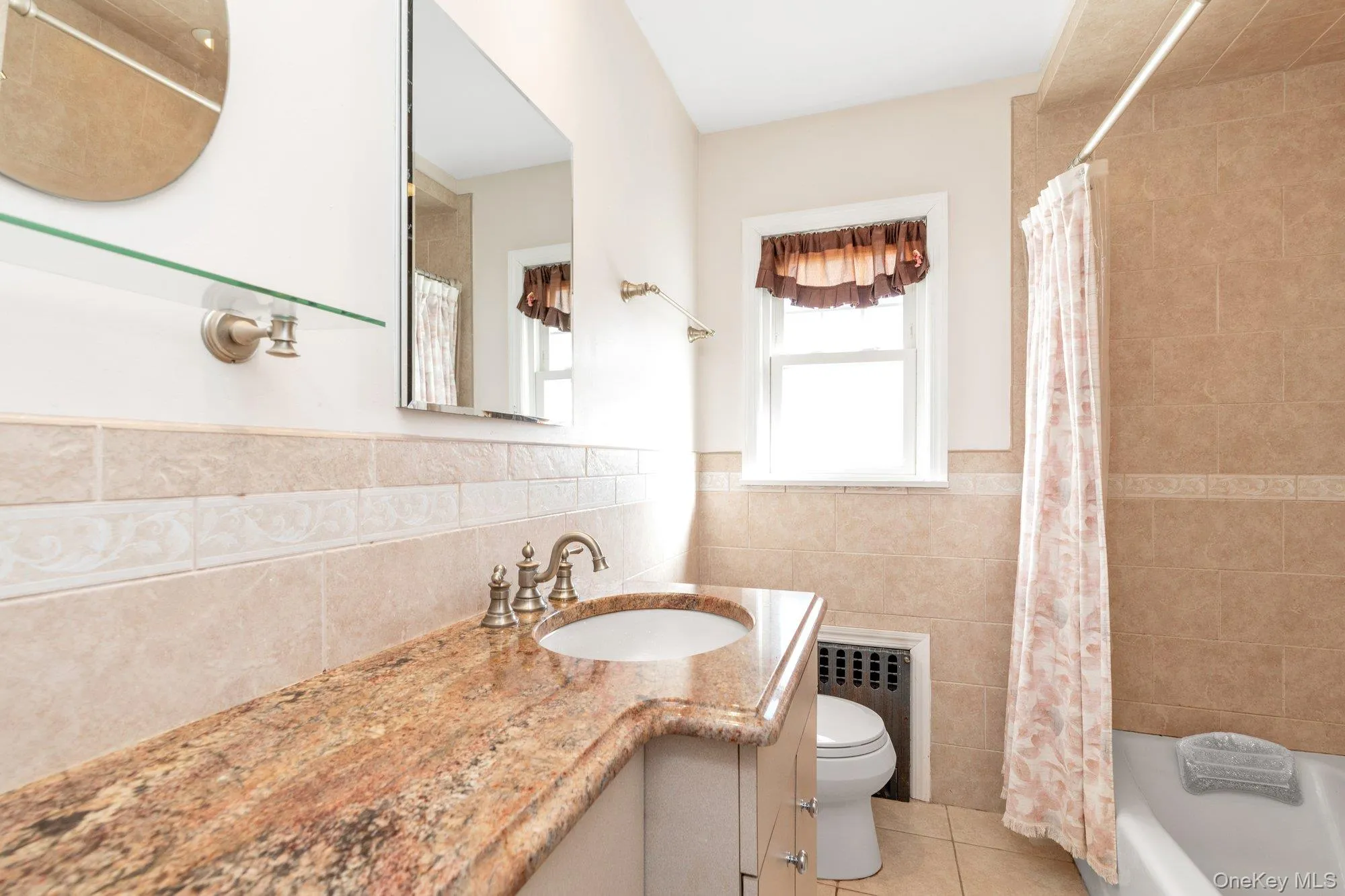 Full bath with vanity, light tile patterned flooring, radiator heating unit, tile walls, and a wainscoted wall Full bath with vanity, light tile patterned flooring, radiator heating unit, tile walls, and a wainscoted wall