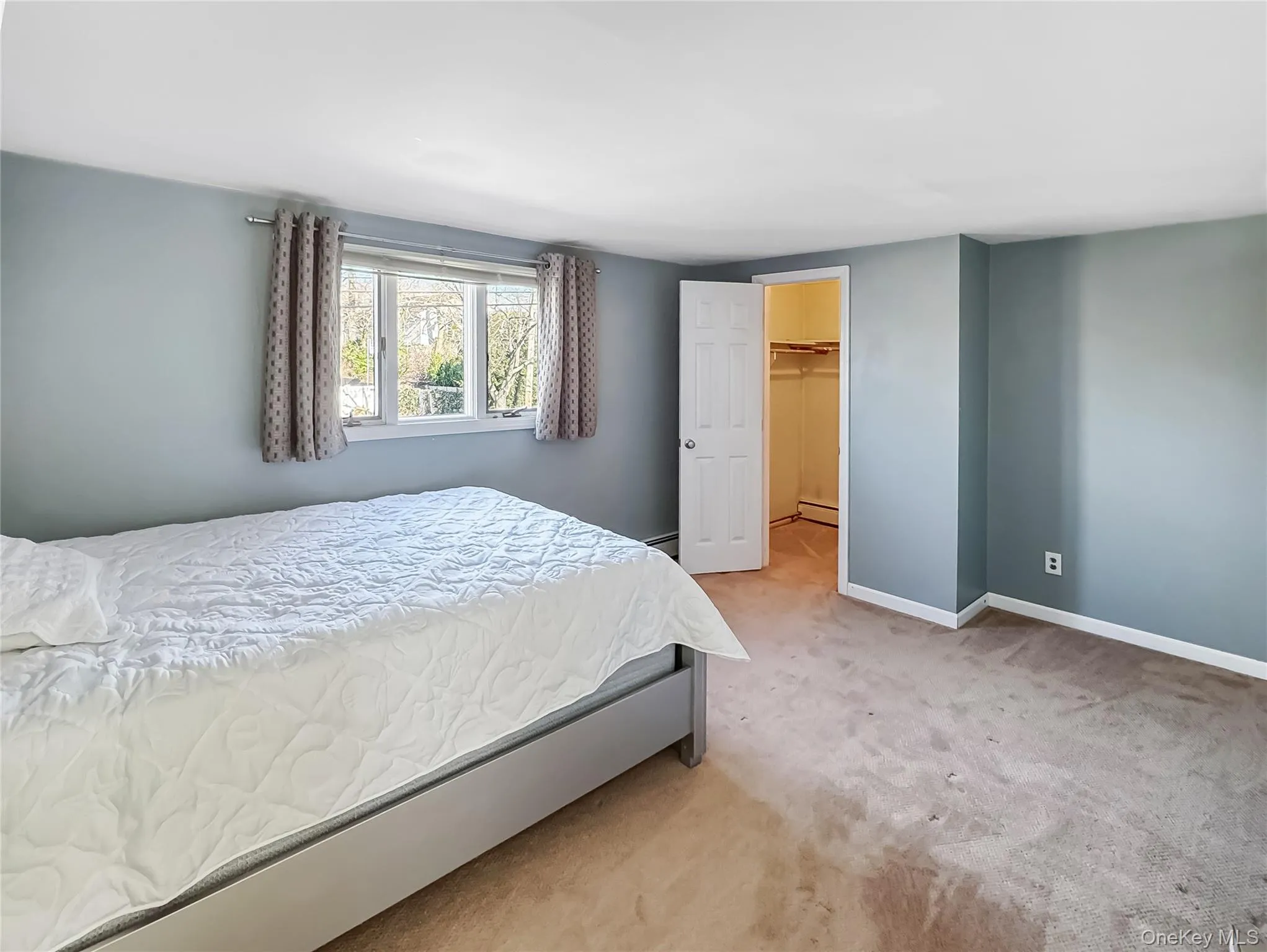 Carpeted bedroom with a spacious closet and a baseboard heating unit Carpeted bedroom with a spacious closet and a baseboard heating unit