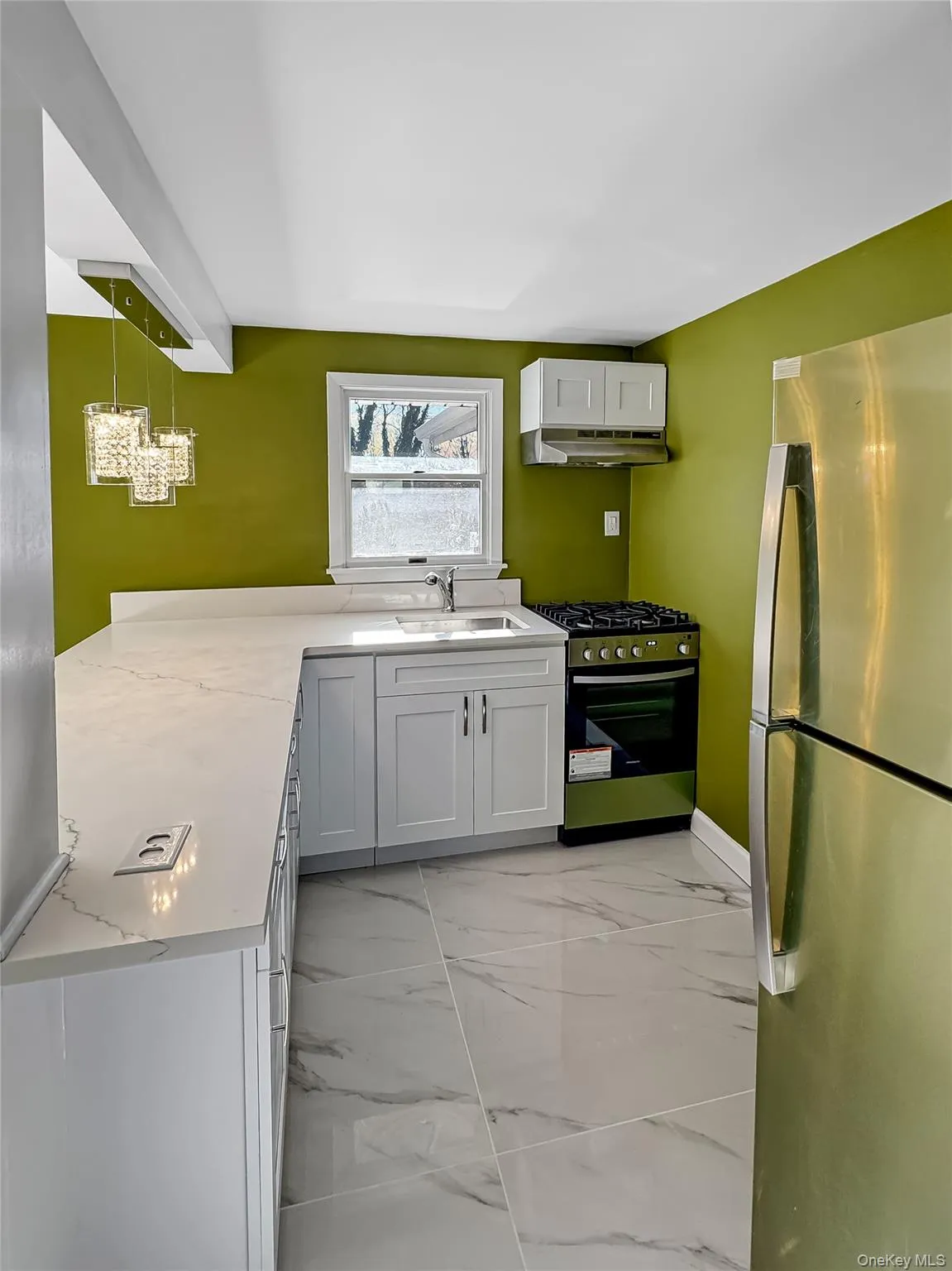 Kitchen featuring stainless steel appliances, light marble finish flooring, white cabinets, under cabinet range hood, and a peninsula Kitchen featuring stainless steel appliances, light marble finish flooring, white cabinets, under cabinet range hood, and a peninsula