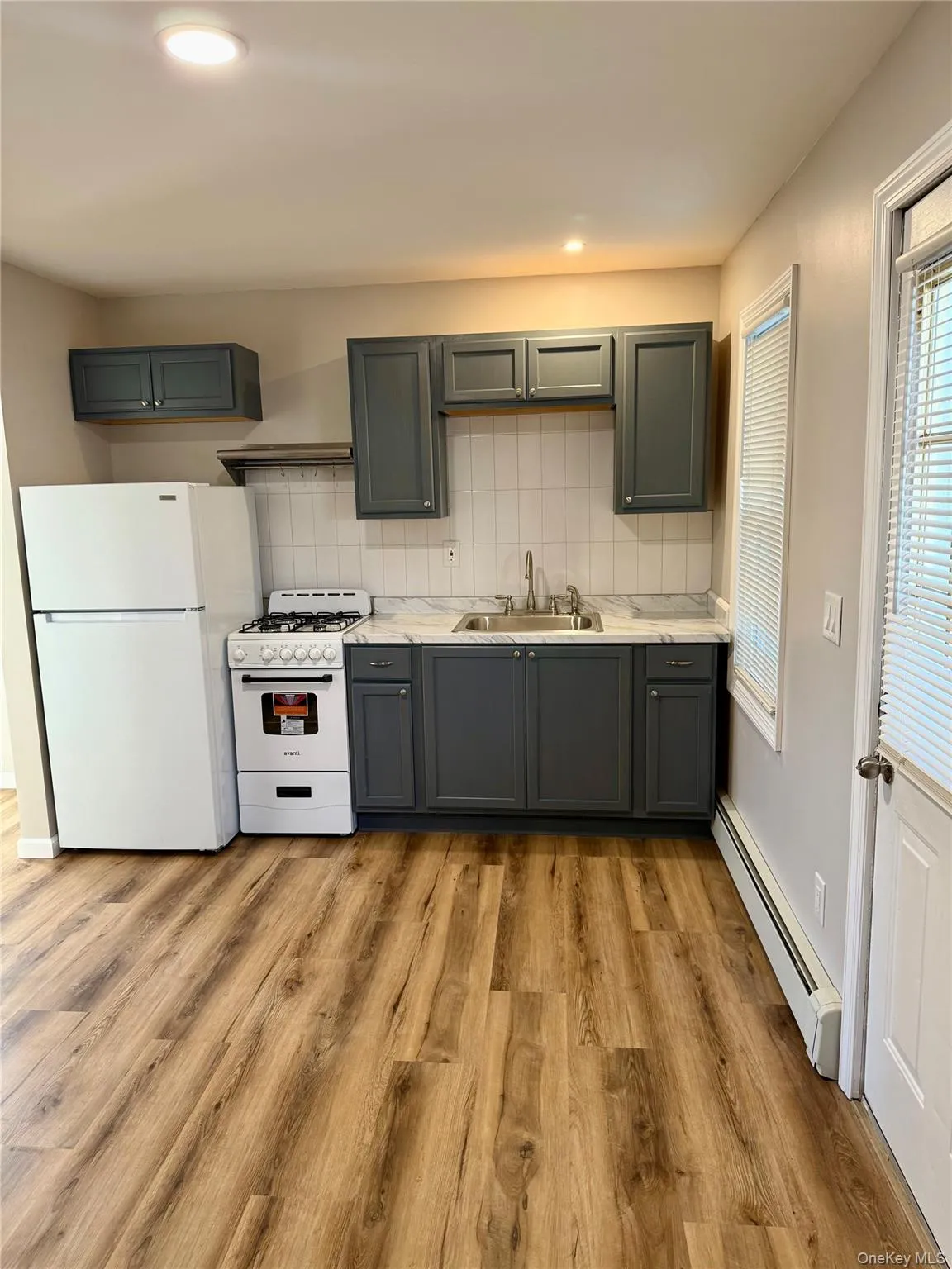 Kitchen featuring white appliances, decorative backsplash, baseboard heating, gray cabinetry, and light countertops Kitchen featuring white appliances, decorative backsplash, baseboard heating, gray cabinetry, and light countertops