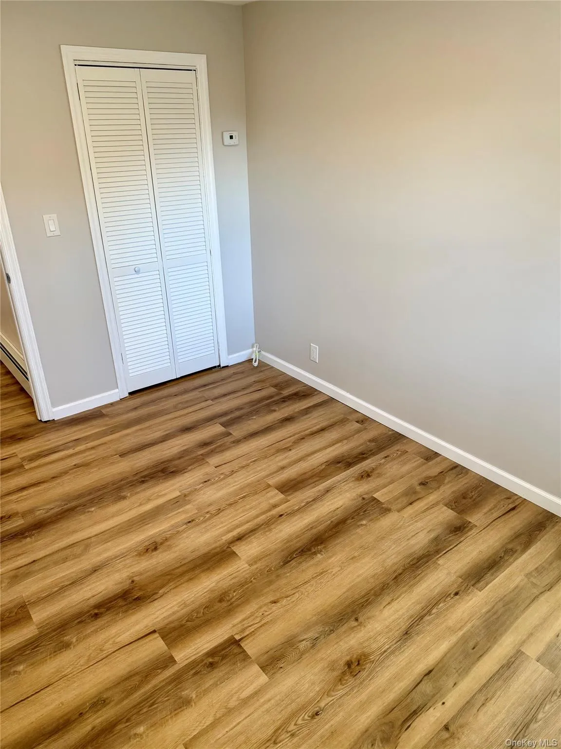 Unfurnished bedroom with wood finished floors, a closet, and a baseboard radiator Unfurnished bedroom with wood finished floors, a closet, and a baseboard radiator