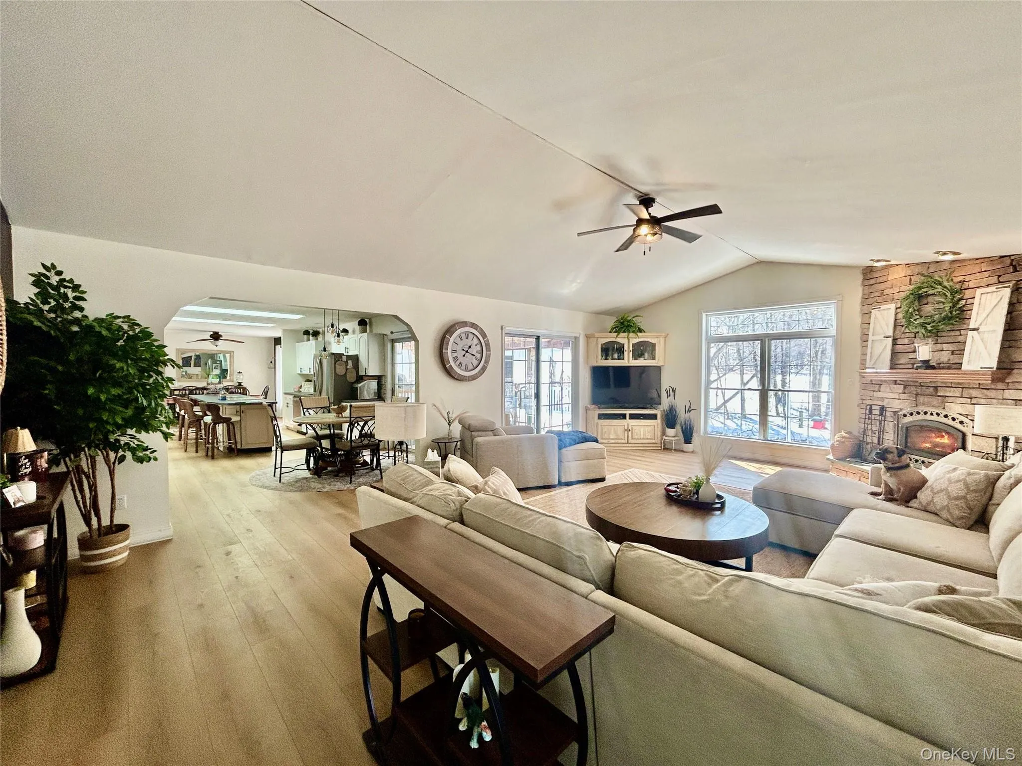 Living room featuring ceiling fan, arched walkways, hardwood / wood-style floors, and a stone fireplace Living room featuring ceiling fan, arched walkways, hardwood / wood-style floors, and a stone fireplace