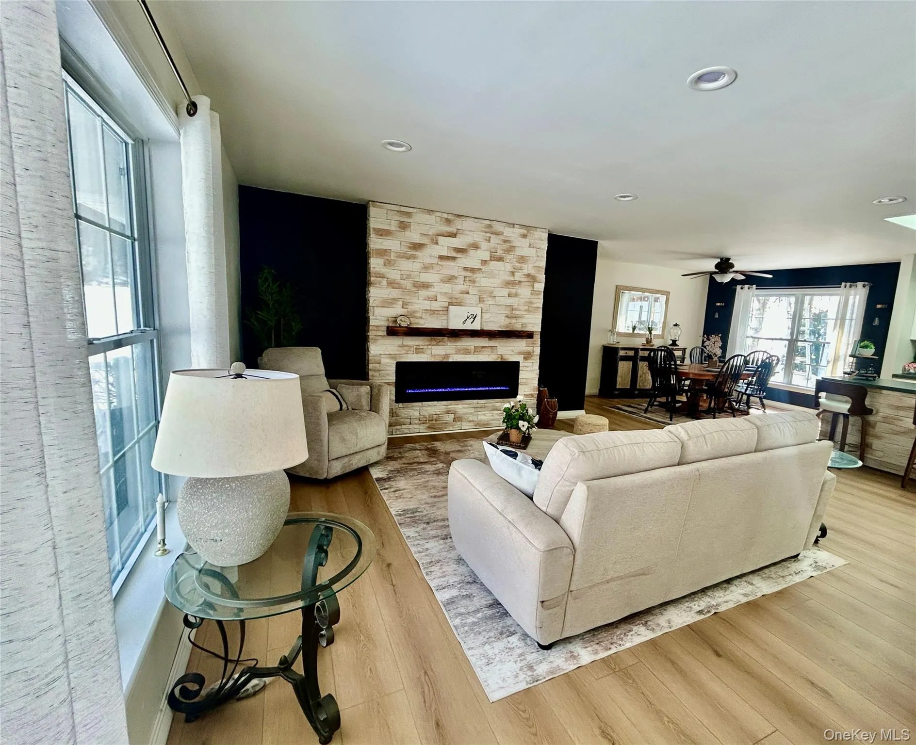 Living room featuring a stone fireplace, light wood finished floors, a ceiling fan, and recessed lighting Living room featuring a stone fireplace, light wood finished floors, a ceiling fan, and recessed lighting