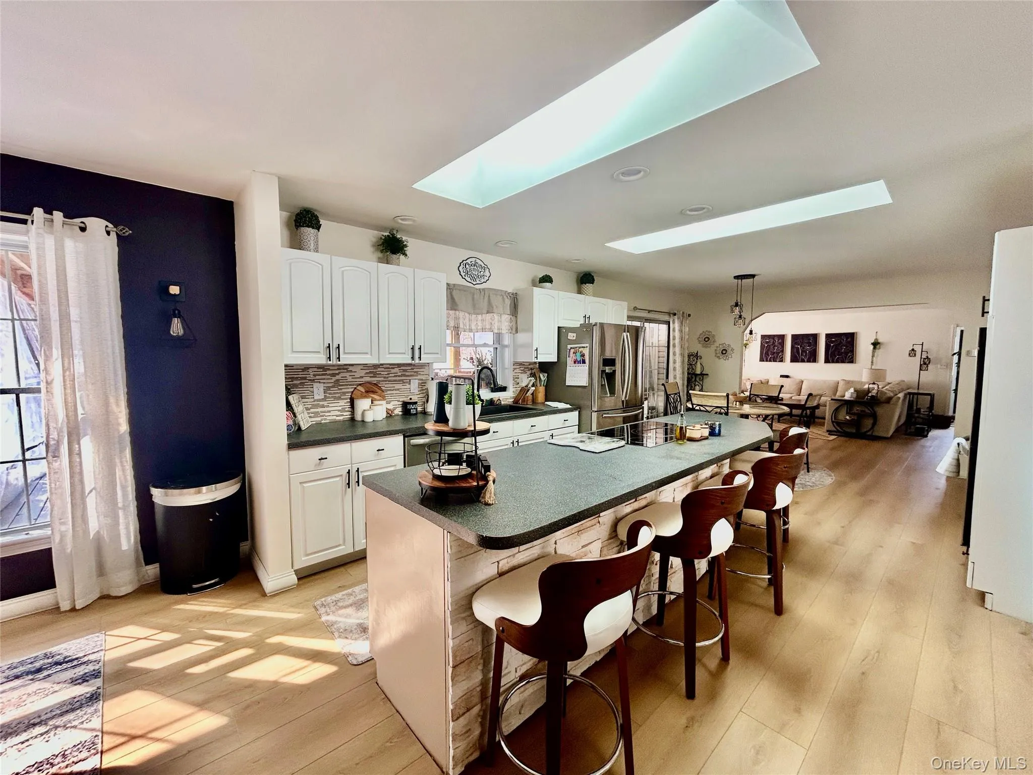 Kitchen with a skylight, a breakfast bar, dark countertops, stainless steel fridge with ice dispenser, and white cabinets Kitchen with a skylight, a breakfast bar, dark countertops, stainless steel fridge with ice dispenser, and white cabinets