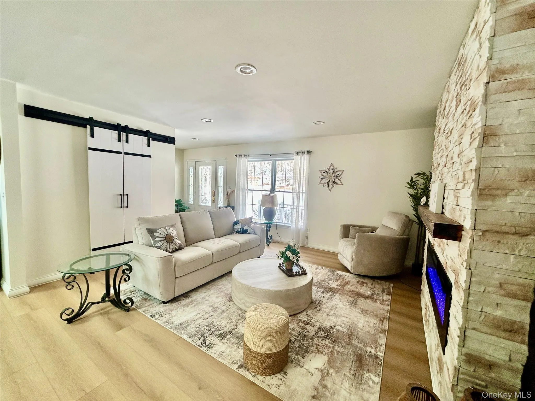 Living room featuring a barn door, light wood-type flooring, and a stone fireplace Living room featuring a barn door, light wood-type flooring, and a stone fireplace