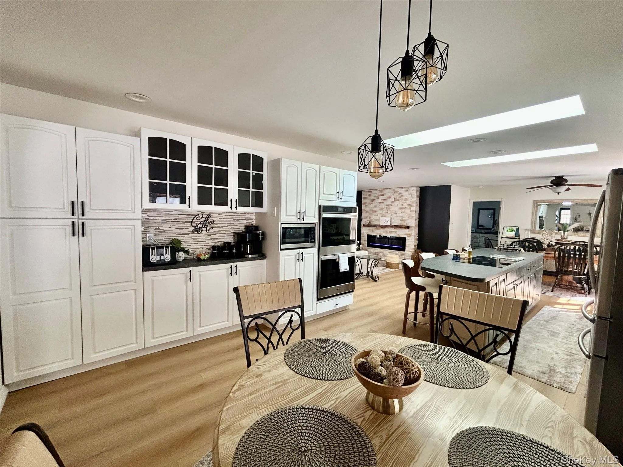 Dining area with light wood-type flooring, a large fireplace, a ceiling fan, and a skylight Dining area with light wood-type flooring, a large fireplace, a ceiling fan, and a skylight