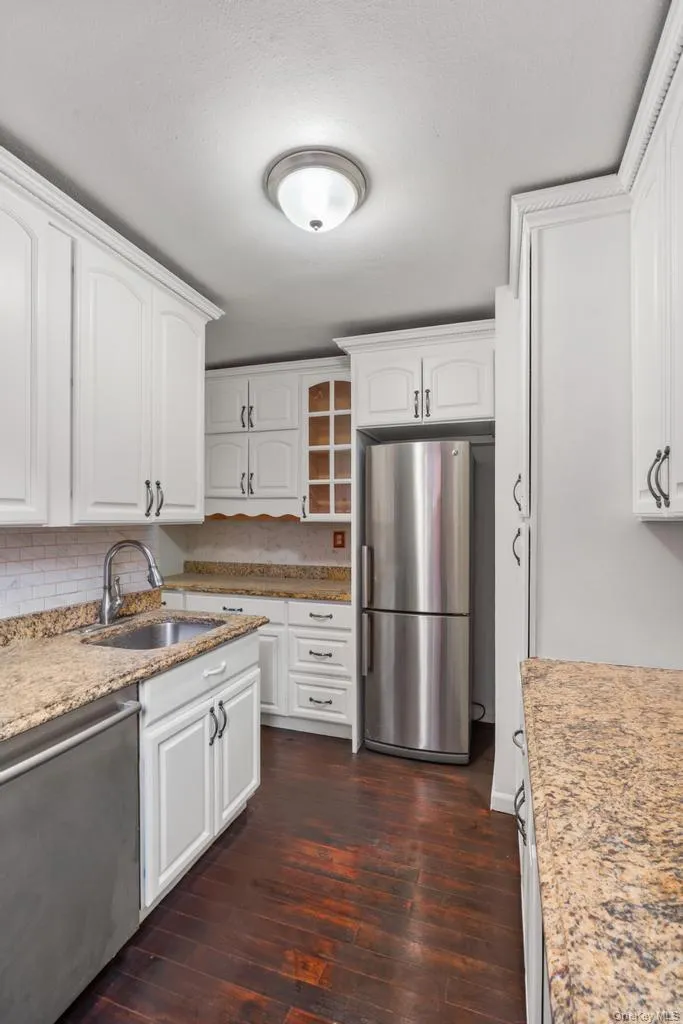 Kitchen with stainless steel appliances, light stone counters, white cabinets, dark wood finished floors, and glass insert cabinets Kitchen with stainless steel appliances, light stone counters, white cabinets, dark wood finished floors, and glass insert cabinets