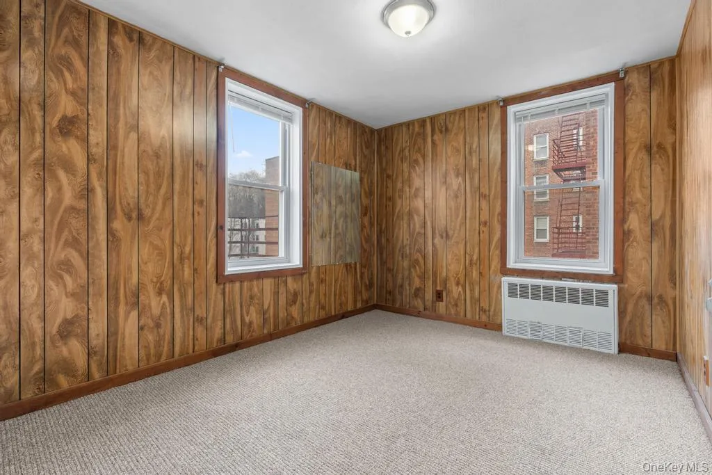 Unfurnished room with radiator, light colored carpet, and wood walls Unfurnished room with radiator, light colored carpet, and wood walls