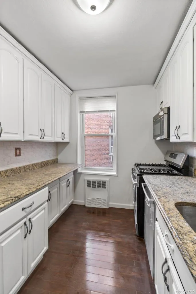 Kitchen with white cabinetry, light stone countertops, appliances with stainless steel finishes, dark wood finished floors, and backsplash Kitchen with white cabinetry, light stone countertops, appliances with stainless steel finishes, dark wood finished floors, and backsplash
