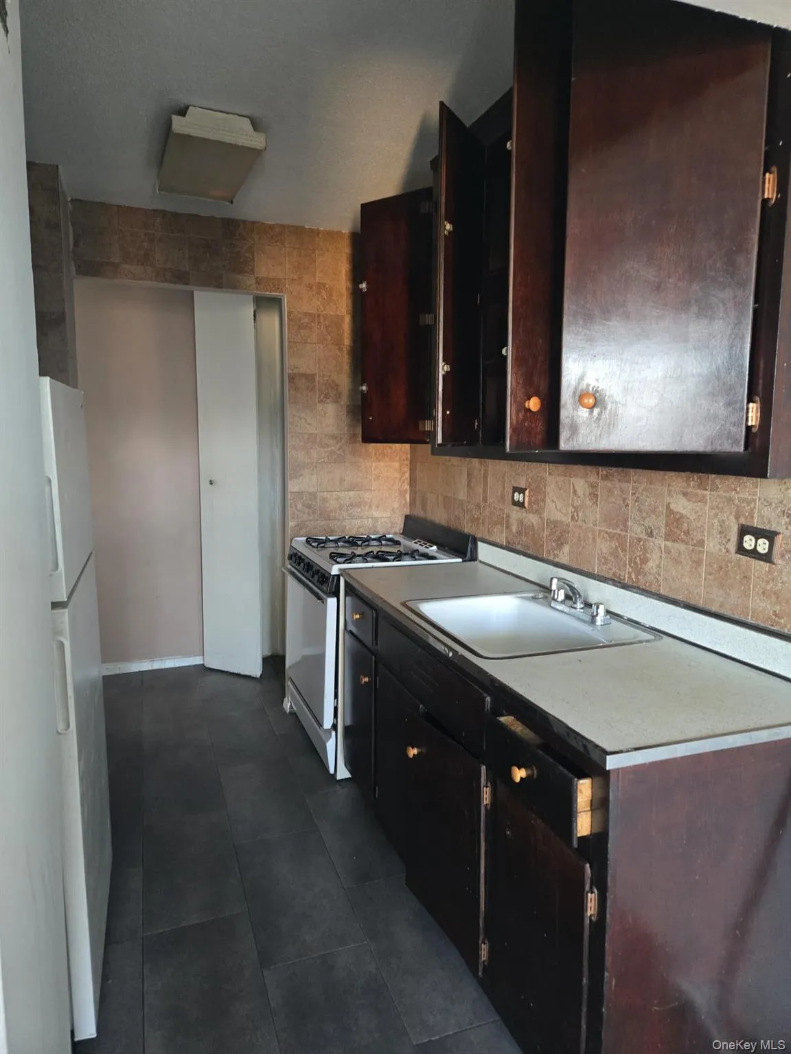 Kitchen with white appliances, light countertops, backsplash, tile walls, and dark brown cabinets Kitchen with white appliances, light countertops, backsplash, tile walls, and dark brown cabinets