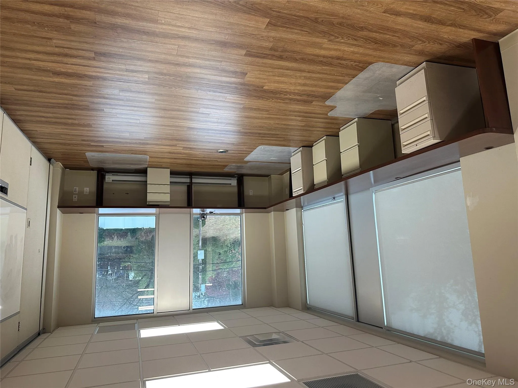 Unfurnished office featuring built in desk, light wood finished floors, a drop ceiling, and a baseboard heating unit Unfurnished office featuring built in desk, light wood finished floors, a drop ceiling, and a baseboard heating unit