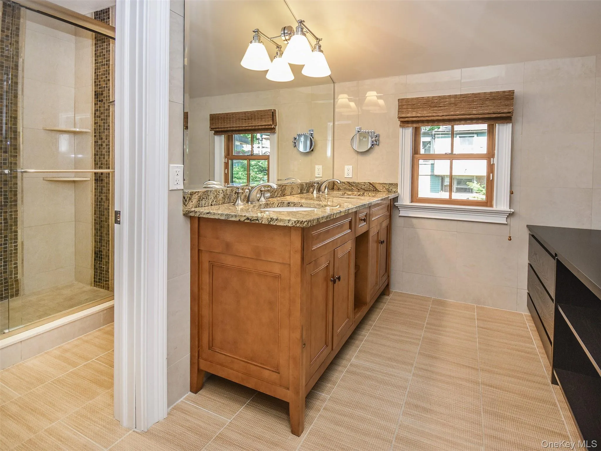 En Suite bathroom featuring double vanity, plenty of natural light, a chandelier, tile walls, and light tile patterned floors En Suite bathroom featuring double vanity, plenty of natural light, a chandelier, tile walls, and light tile patterned floors