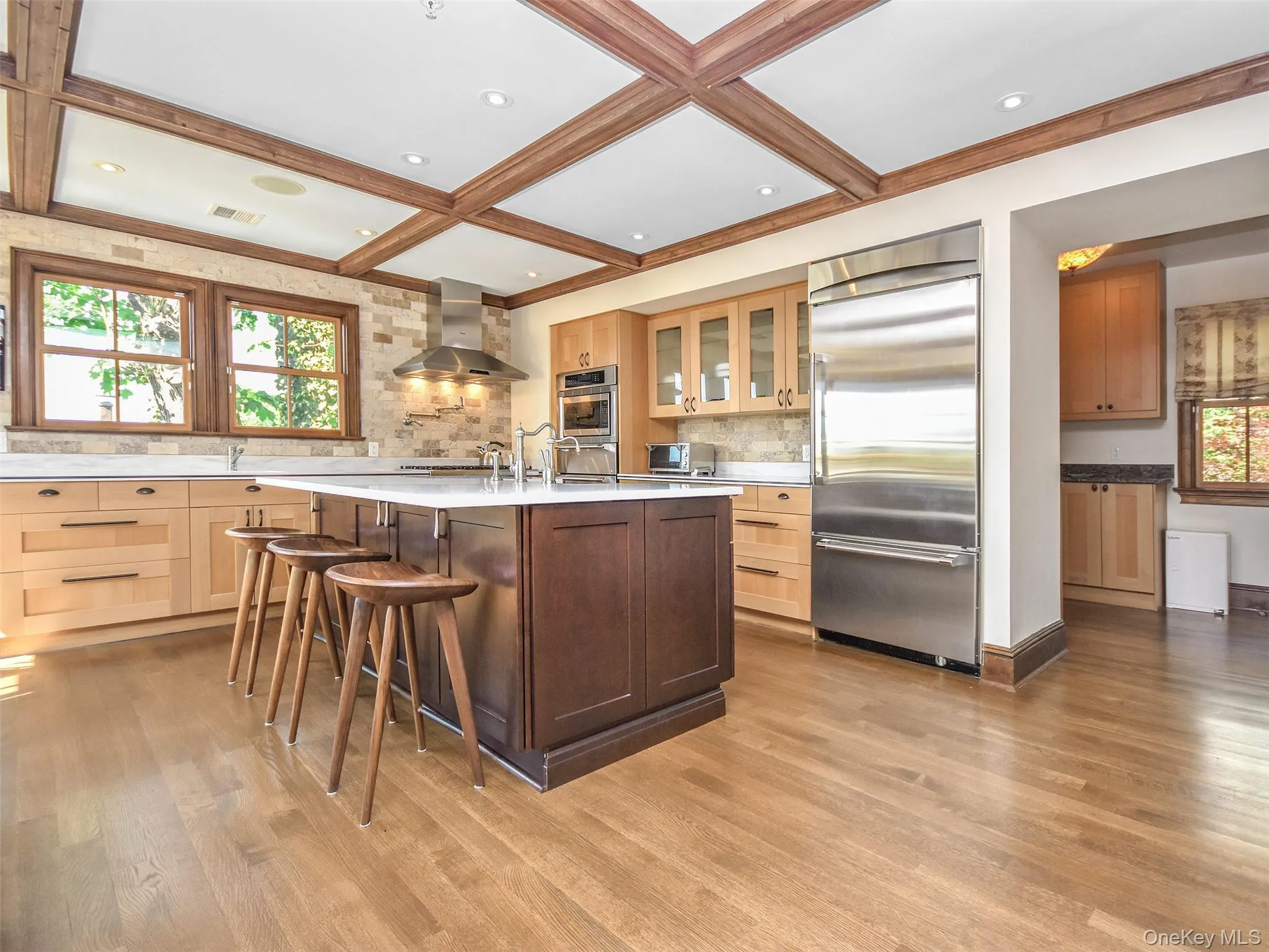 Kitchen featuring a breakfast bar area, glass insert cabinets, stainless steel appliances, gas cooking an island with sink, and wall chimney exhaust hood Kitchen featuring a breakfast bar area, glass insert cabinets, stainless steel appliances, gas cooking an island with sink, and wall chimney exhaust hood