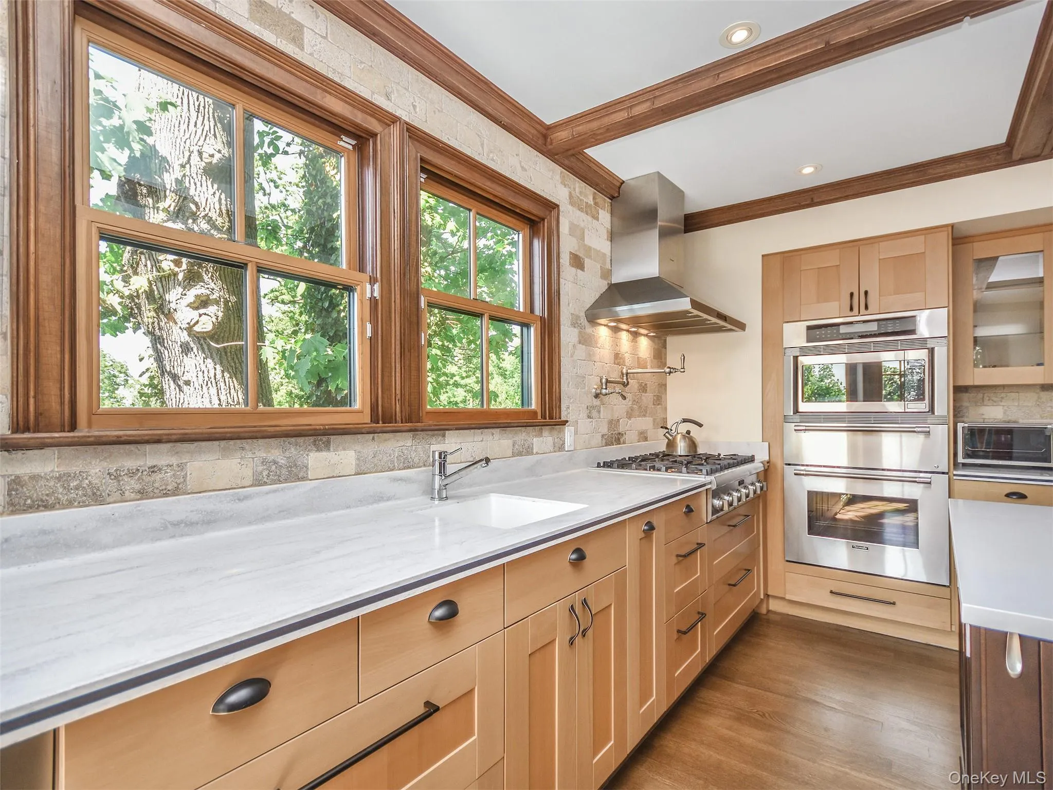 Kitchen with exhaust hood over gas stove top, double oven, dark wood-style floors, glass insert cabinets, light stone counters, and crown molding Kitchen with exhaust hood over gas stove top, double oven, dark wood-style floors, glass insert cabinets, light stone counters, and crown molding
