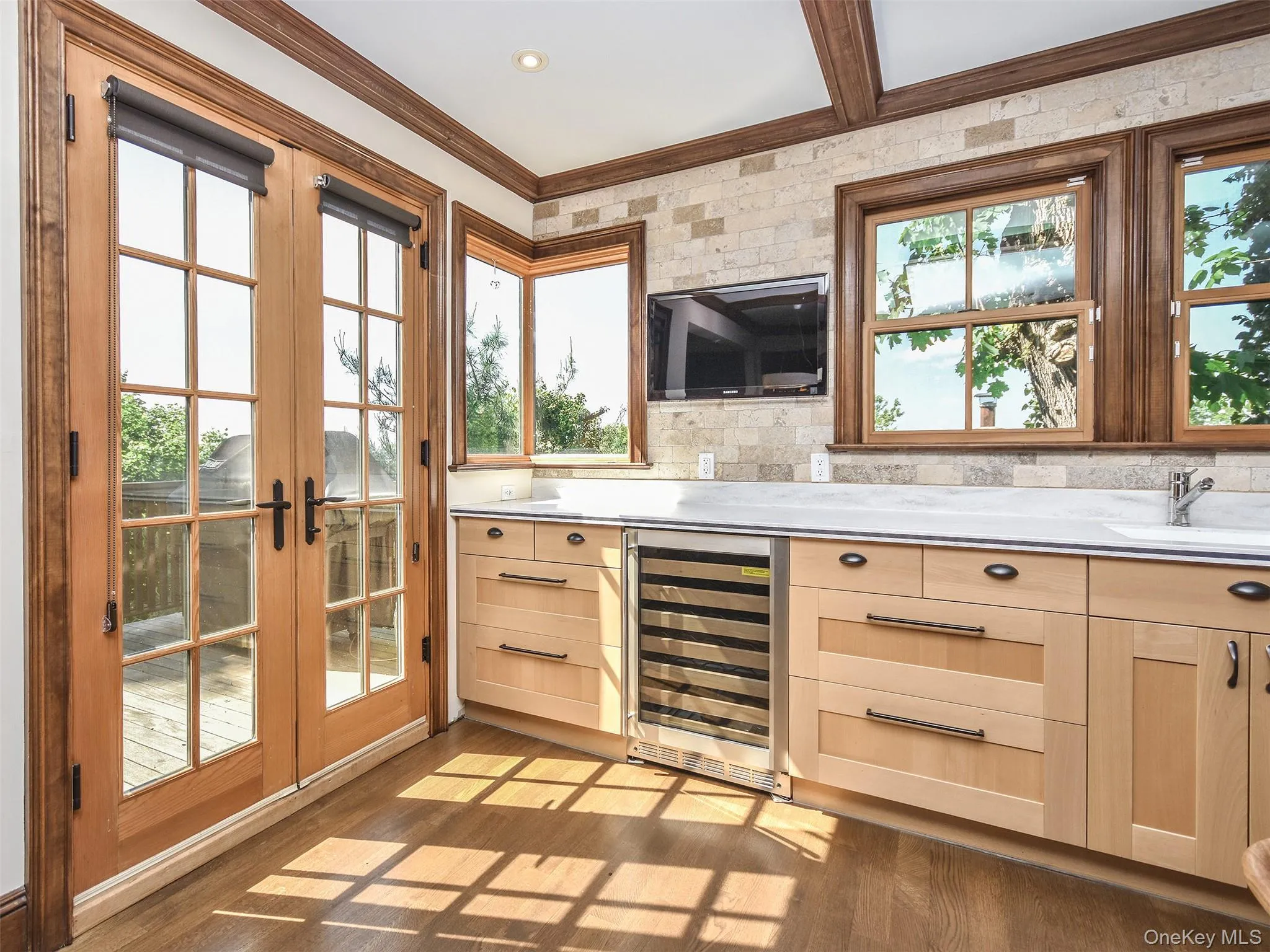 Wall TV, beverage cooler, French doors lead to BBQ on the wrap deck, crown molding, dark wood-style flooring, and light stone counters Wall TV, beverage cooler, French doors lead to BBQ on the wrap deck, crown molding, dark wood-style flooring, and light stone counters