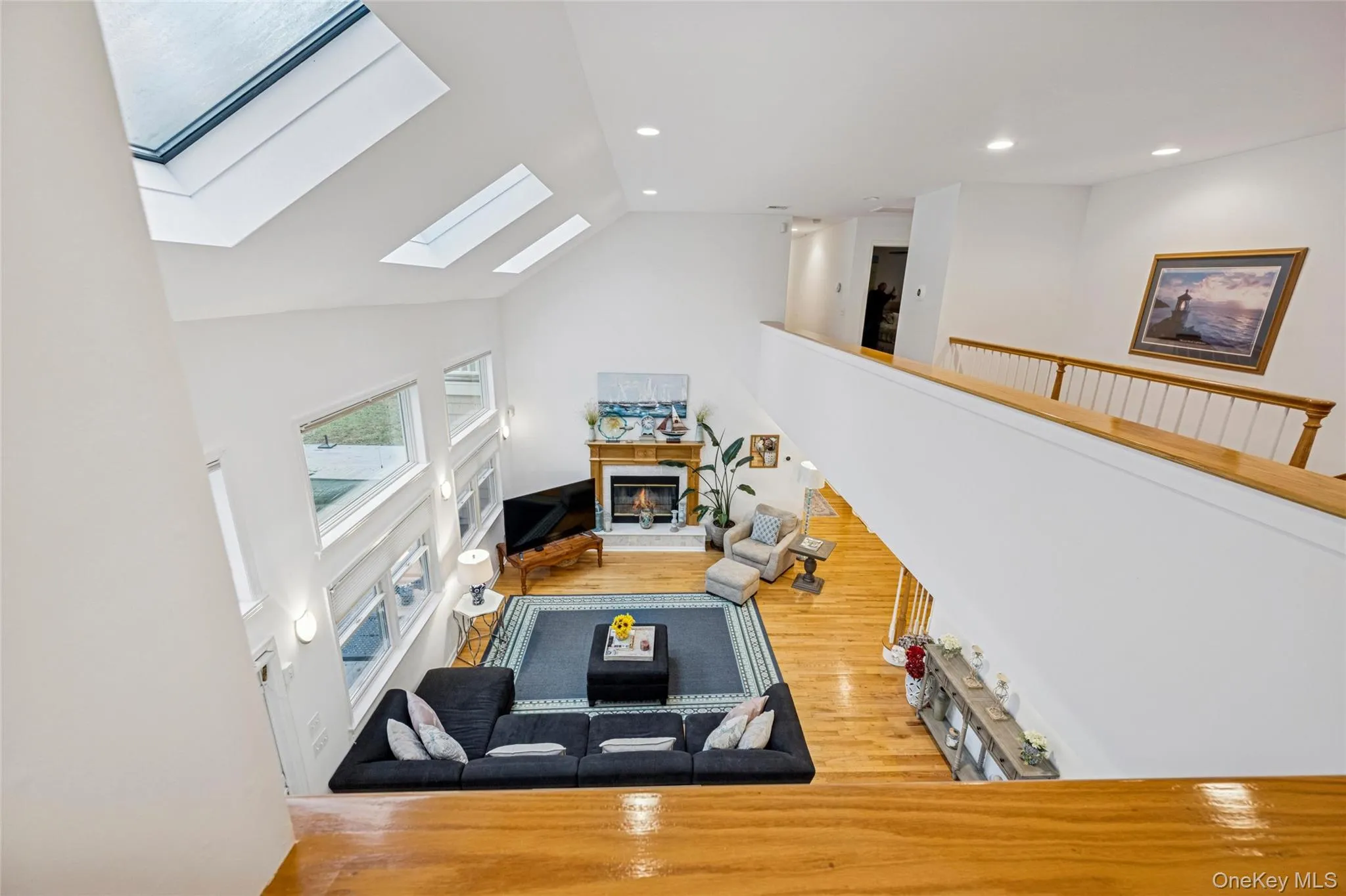 Living area with a glass covered fireplace, a skylight, wood finished floors, recessed lighting, and high vaulted ceiling Living area with a glass covered fireplace, a skylight, wood finished floors, recessed lighting, and high vaulted ceiling