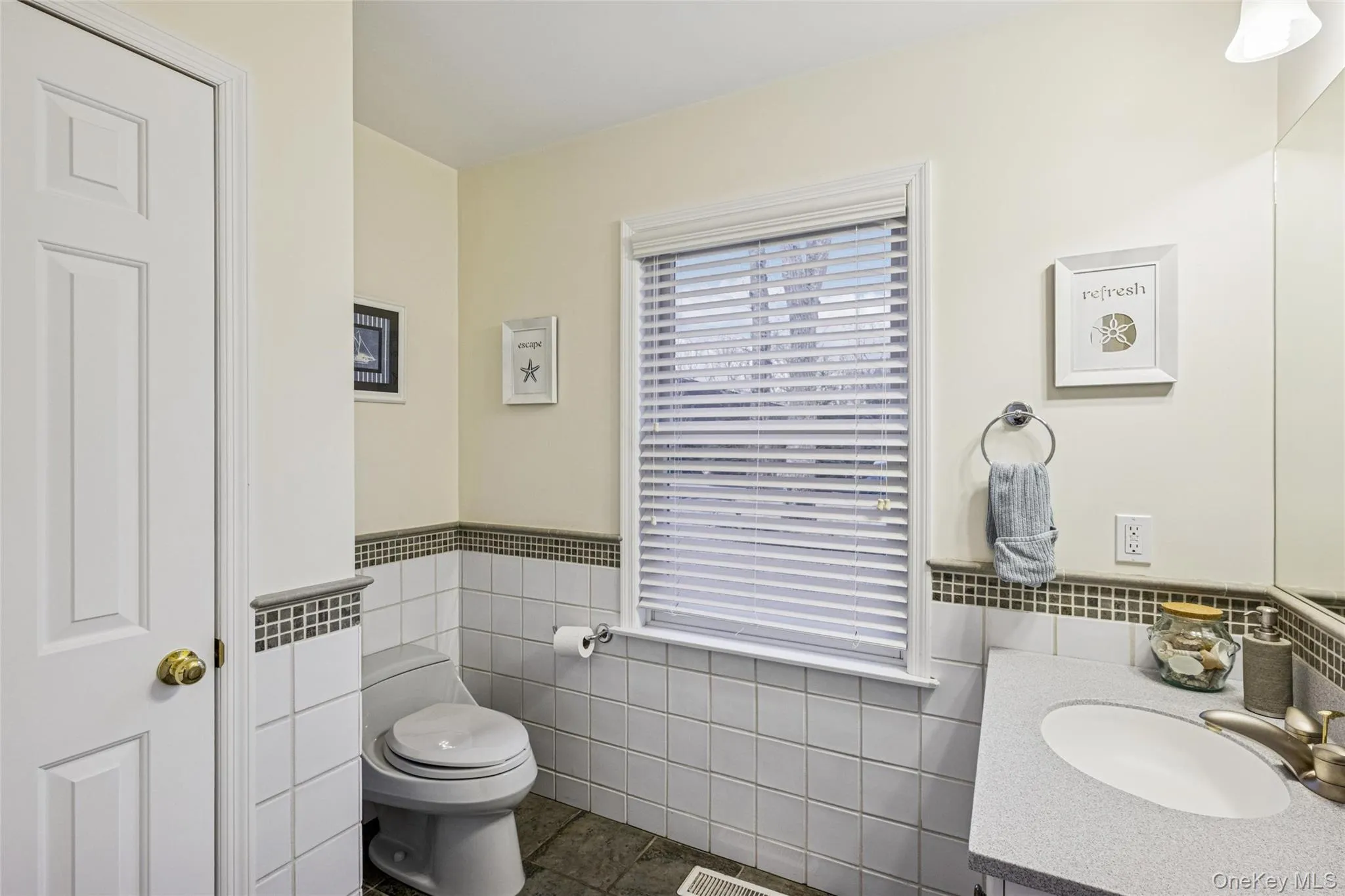 Half bathroom featuring vanity, dark tile patterned floors, a wainscoted wall, and tile walls Half bathroom featuring vanity, dark tile patterned floors, a wainscoted wall, and tile walls