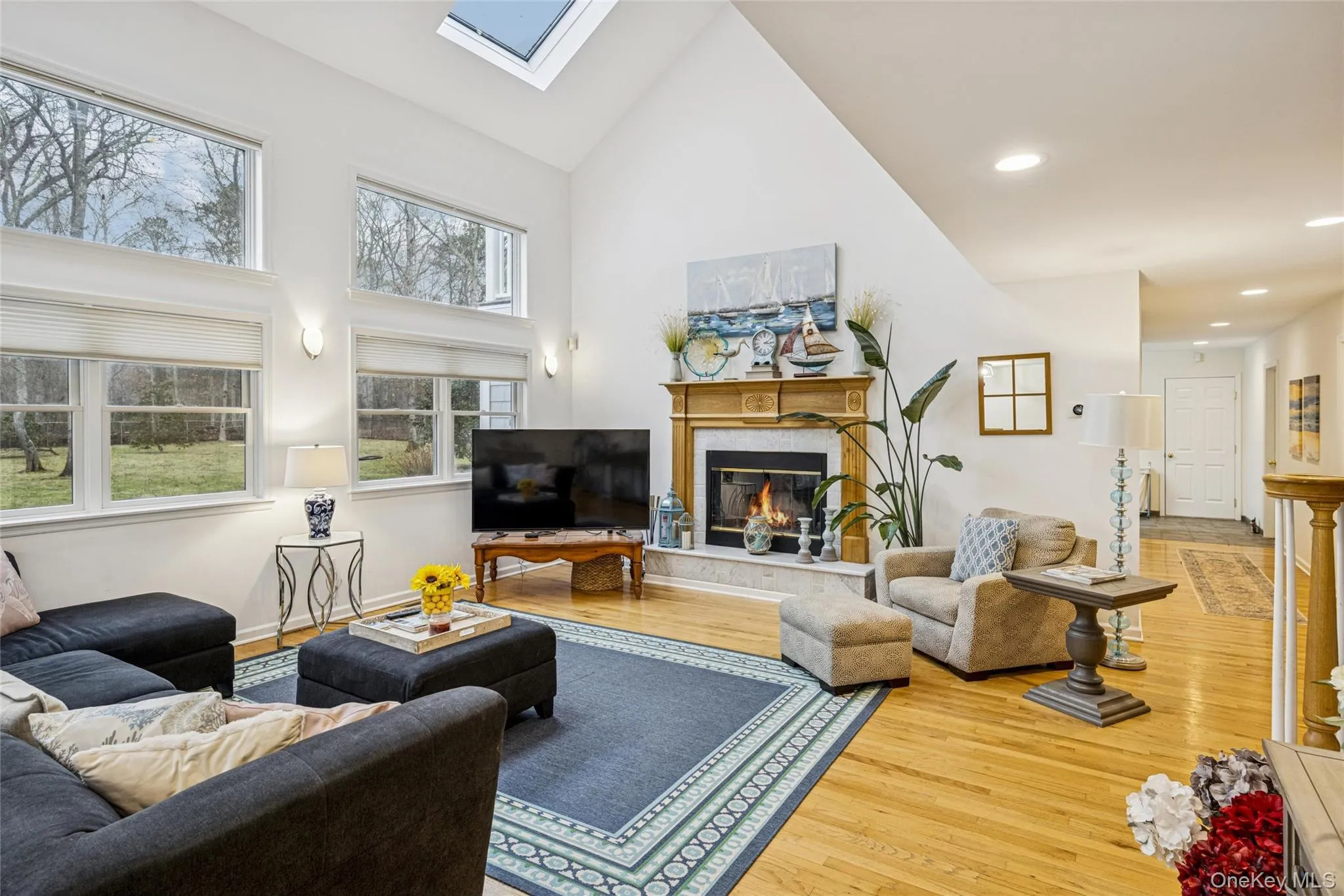 Living area featuring a skylight, a high end fireplace, high vaulted ceiling, and wood finished floors Living area featuring a skylight, a high end fireplace, high vaulted ceiling, and wood finished floors