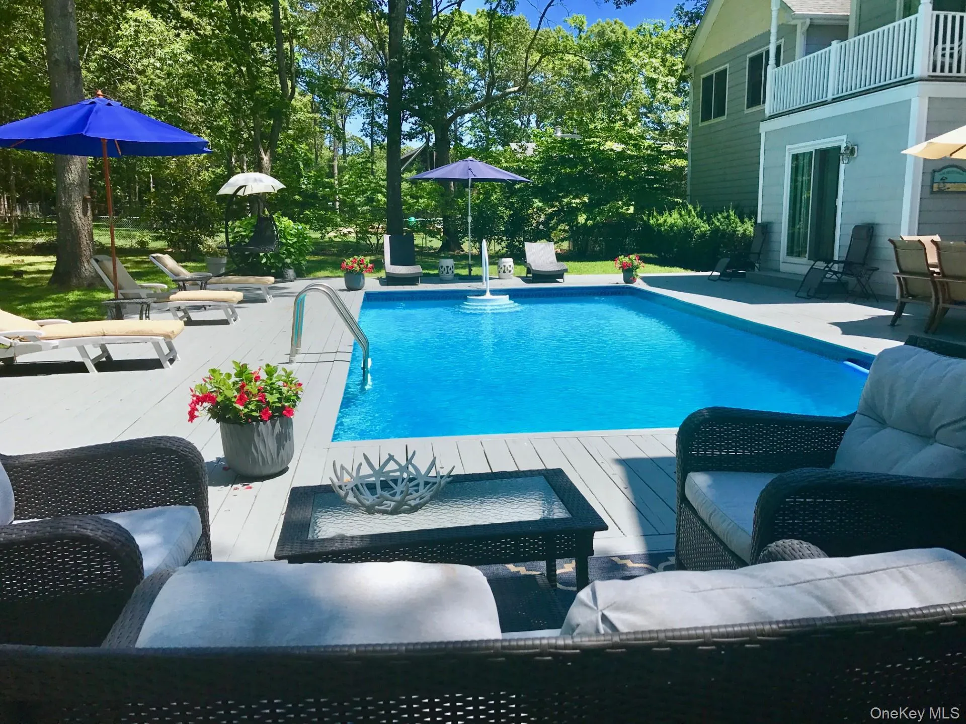 Outdoor pool with an outdoor living space, a wooden deck, a patio, and view of scattered trees Outdoor pool with an outdoor living space, a wooden deck, a patio, and view of scattered trees