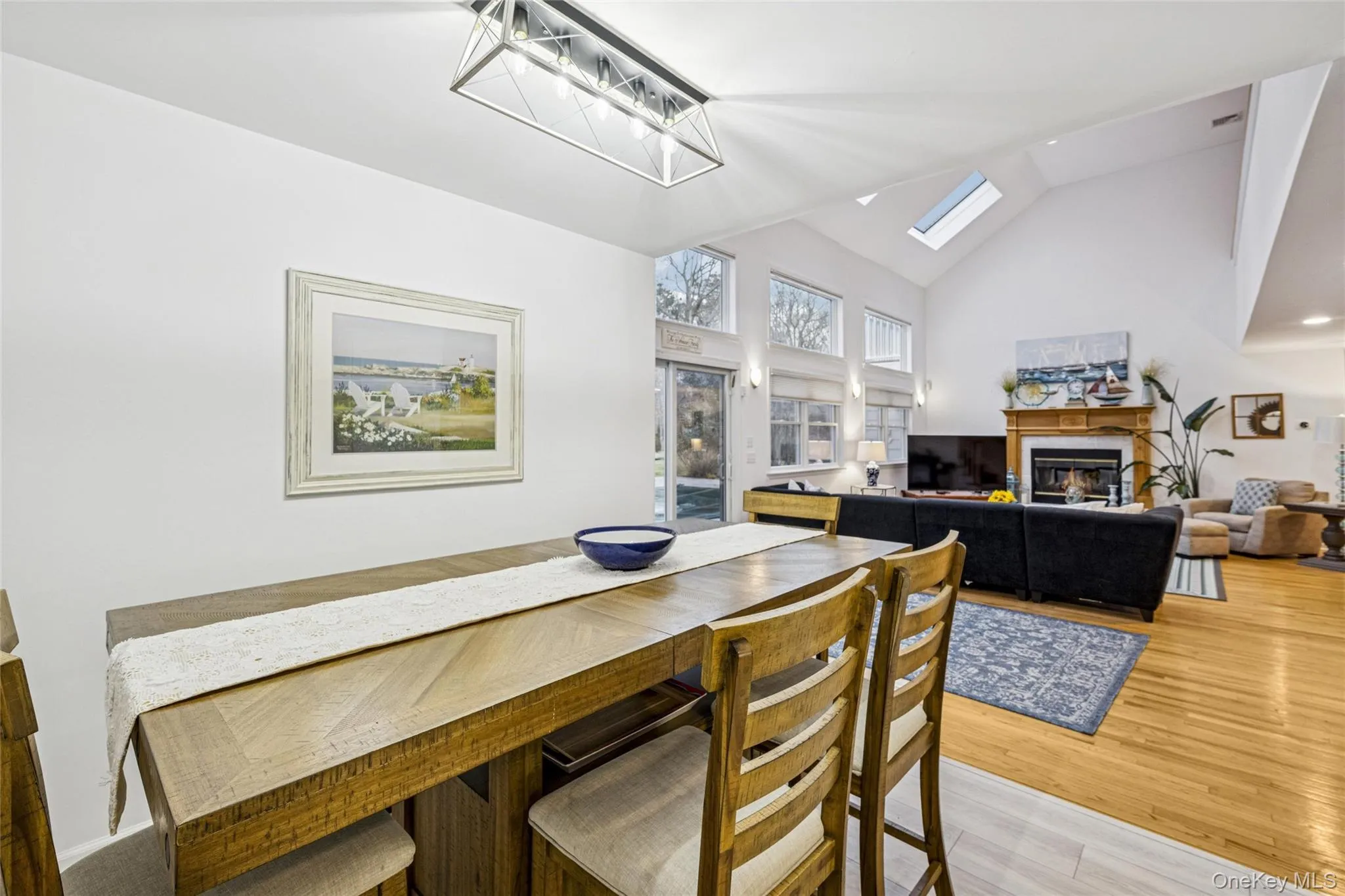 Dining space featuring a glass covered fireplace, high vaulted ceiling, light wood-style floors, and a skylight Dining space featuring a glass covered fireplace, high vaulted ceiling, light wood-style floors, and a skylight