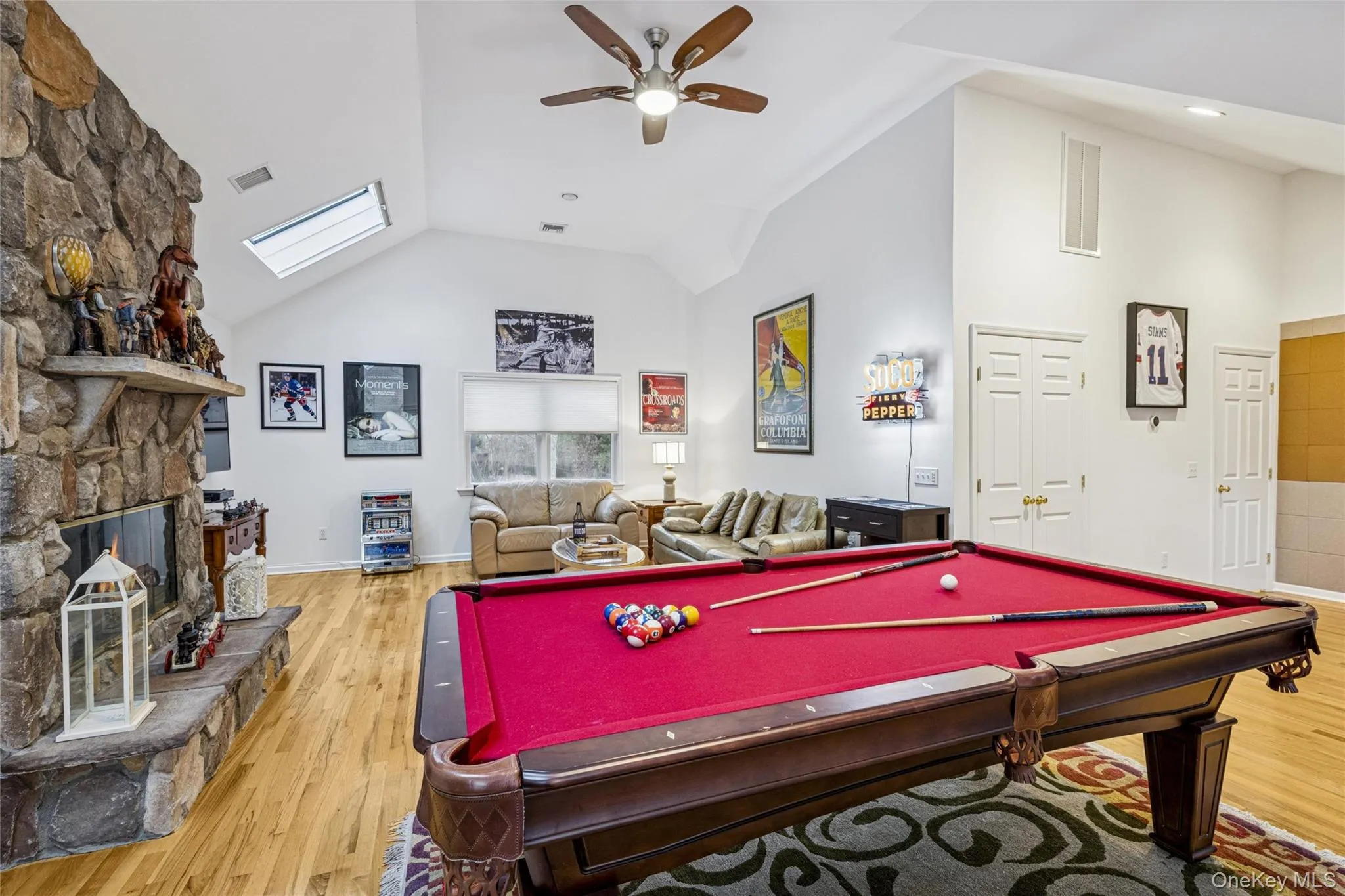 Playroom with a stone fireplace, light wood-style floors, a skylight, high vaulted ceiling, and billiards Playroom with a stone fireplace, light wood-style floors, a skylight, high vaulted ceiling, and billiards