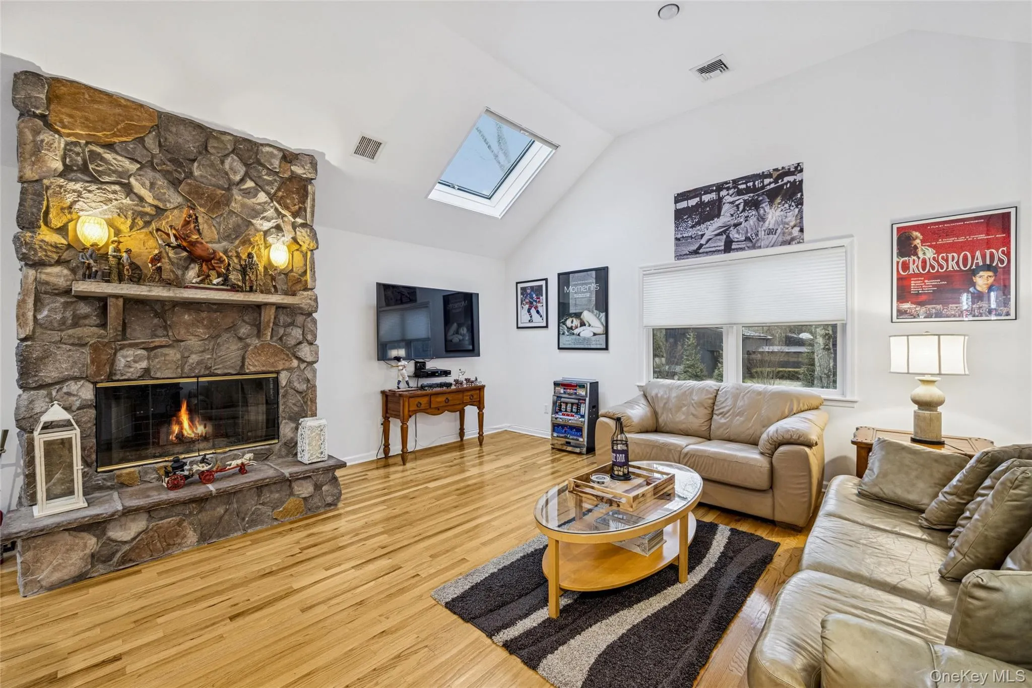 Living room with a stone fireplace, a skylight, lofted ceiling, and wood finished floors Living room with a stone fireplace, a skylight, lofted ceiling, and wood finished floors