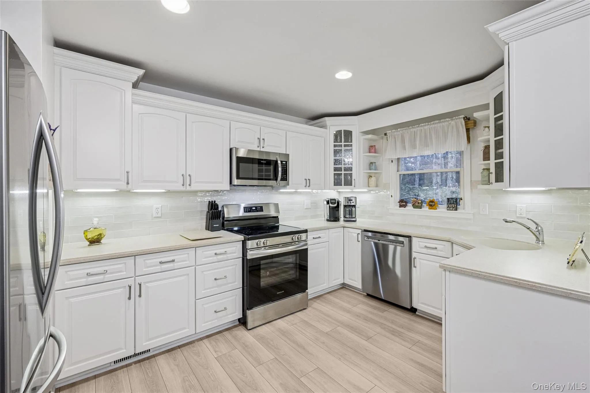 Kitchen featuring appliances with stainless steel finishes, white cabinets, glass insert cabinets, decorative backsplash, and light stone countertops Kitchen featuring appliances with stainless steel finishes, white cabinets, glass insert cabinets, decorative backsplash, and light stone countertops