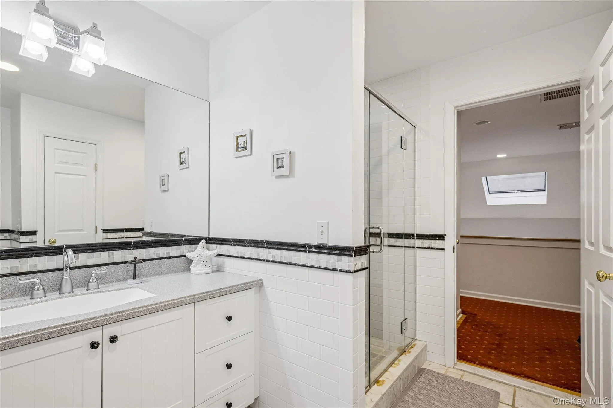 Bathroom featuring vanity, a stall shower, wainscoting, tile walls, and a skylight Bathroom featuring vanity, a stall shower, wainscoting, tile walls, and a skylight