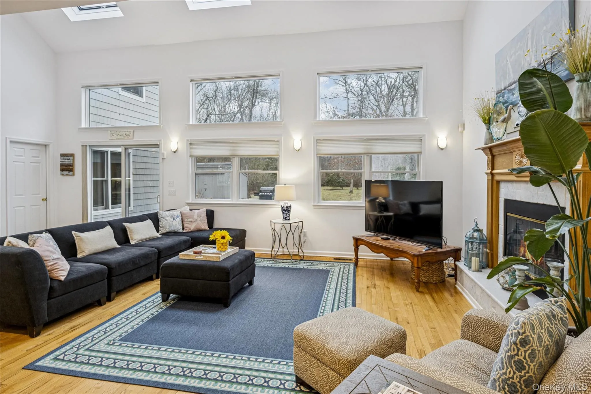 Living room with a towering ceiling, hardwood / wood-style floors, a fireplace, and a skylight Living room with a towering ceiling, hardwood / wood-style floors, a fireplace, and a skylight