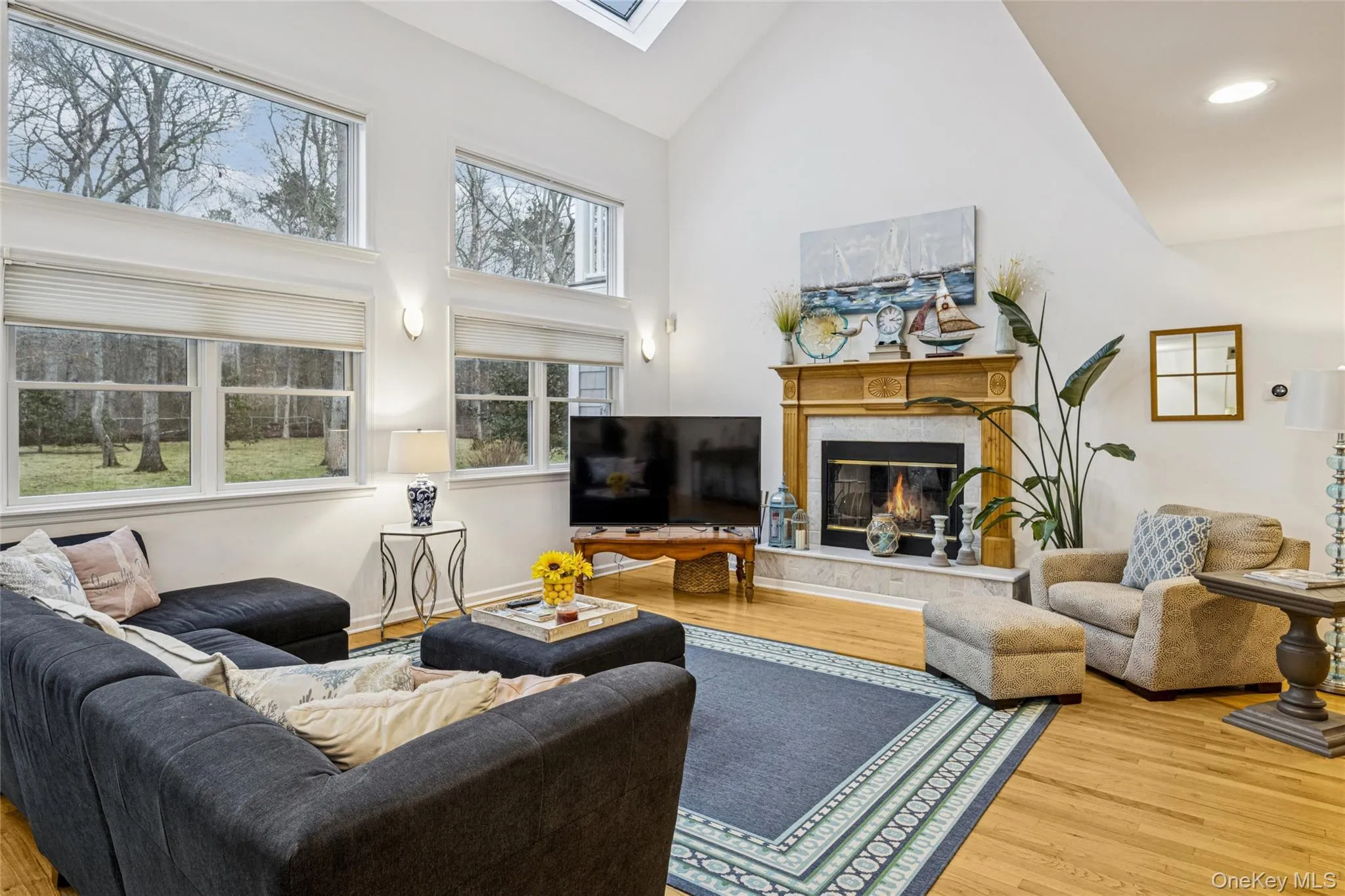 Living area featuring high vaulted ceiling, a skylight, a fireplace, wood finished floors, and recessed lighting Living area featuring high vaulted ceiling, a skylight, a fireplace, wood finished floors, and recessed lighting