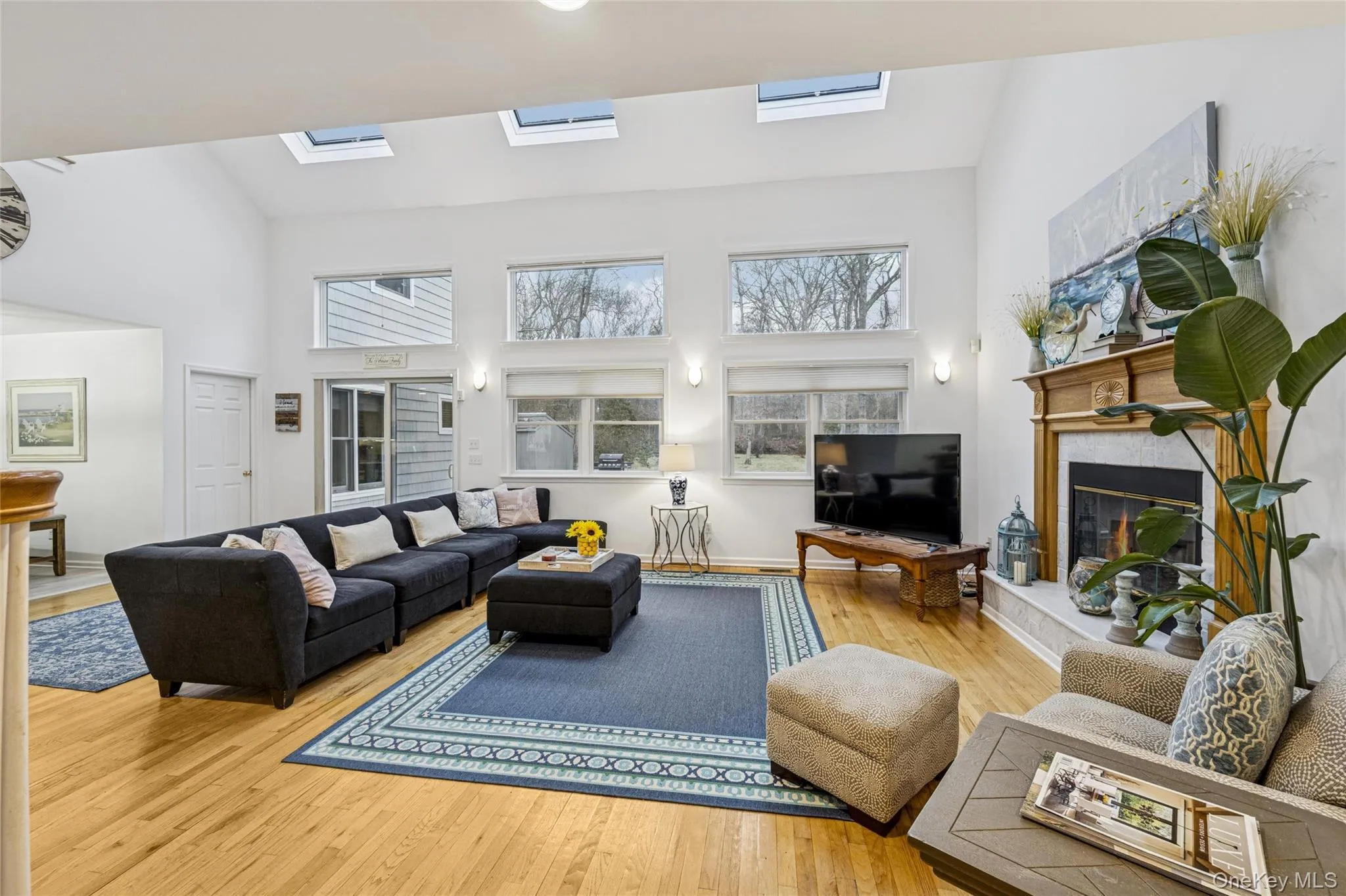 Living room with a glass covered fireplace, light wood-type flooring, high vaulted ceiling, and a skylight Living room with a glass covered fireplace, light wood-type flooring, high vaulted ceiling, and a skylight
