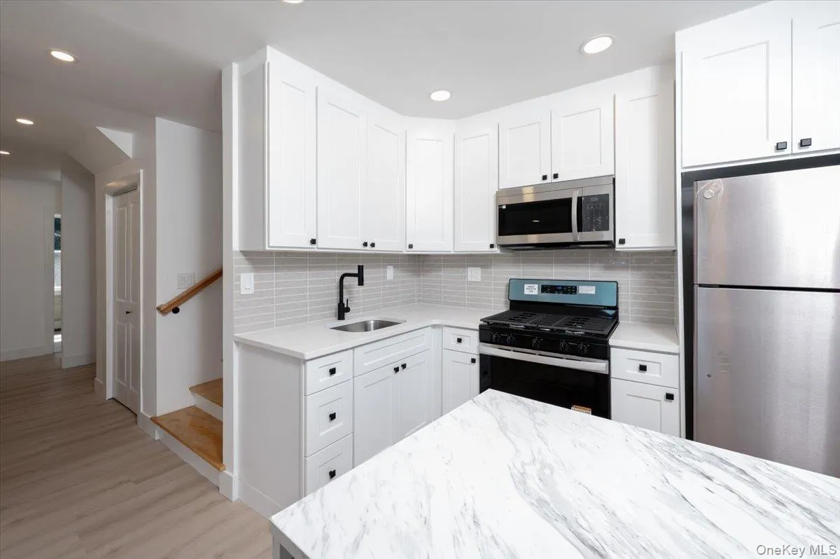 Kitchen featuring appliances with stainless steel finishes, white cabinets, light stone countertops, decorative backsplash, and wood finished floors Kitchen featuring appliances with stainless steel finishes, white cabinets, light stone countertops, decorative backsplash, and wood finished floors