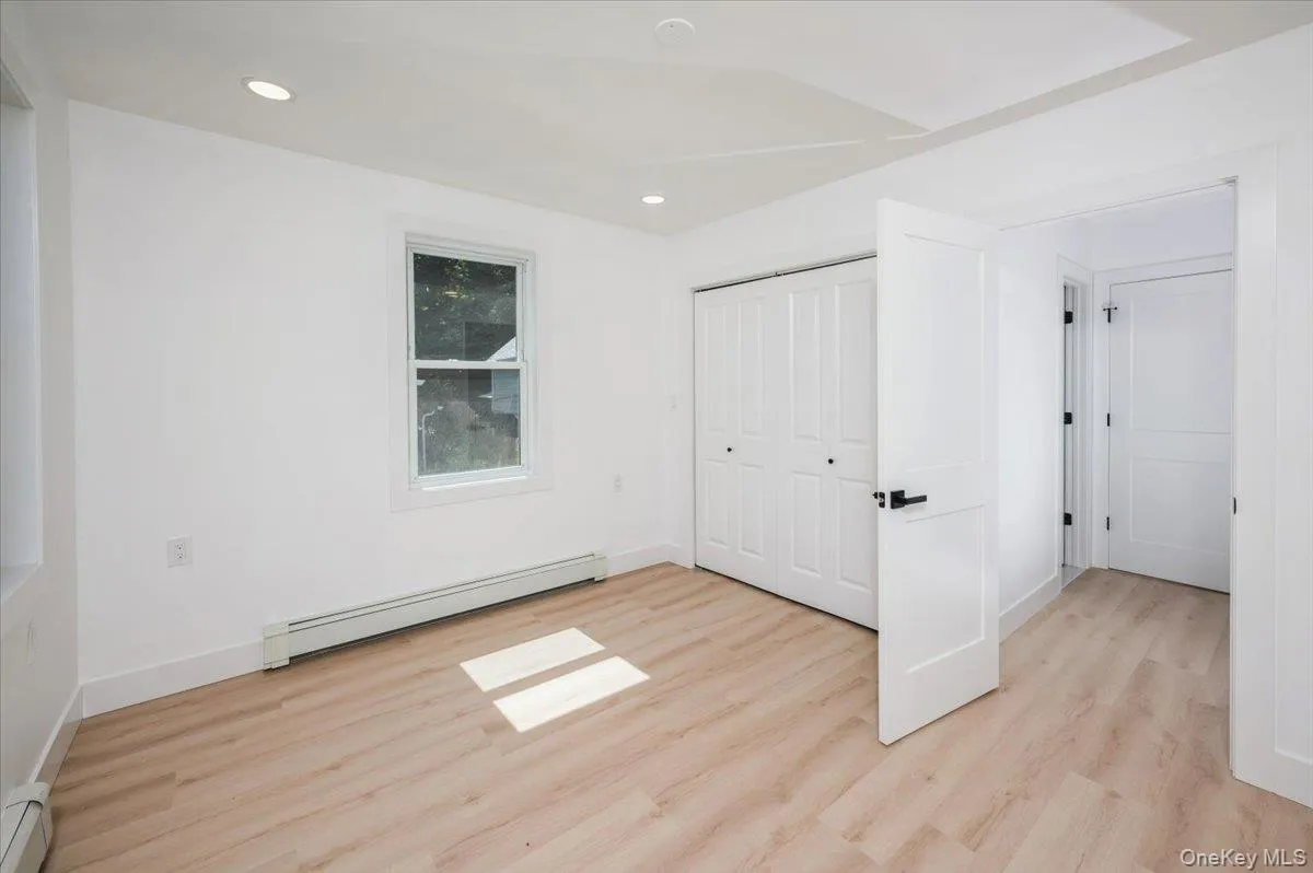 Unfurnished bedroom with a baseboard radiator, light wood finished floors, recessed lighting, and a closet Unfurnished bedroom with a baseboard radiator, light wood finished floors, recessed lighting, and a closet