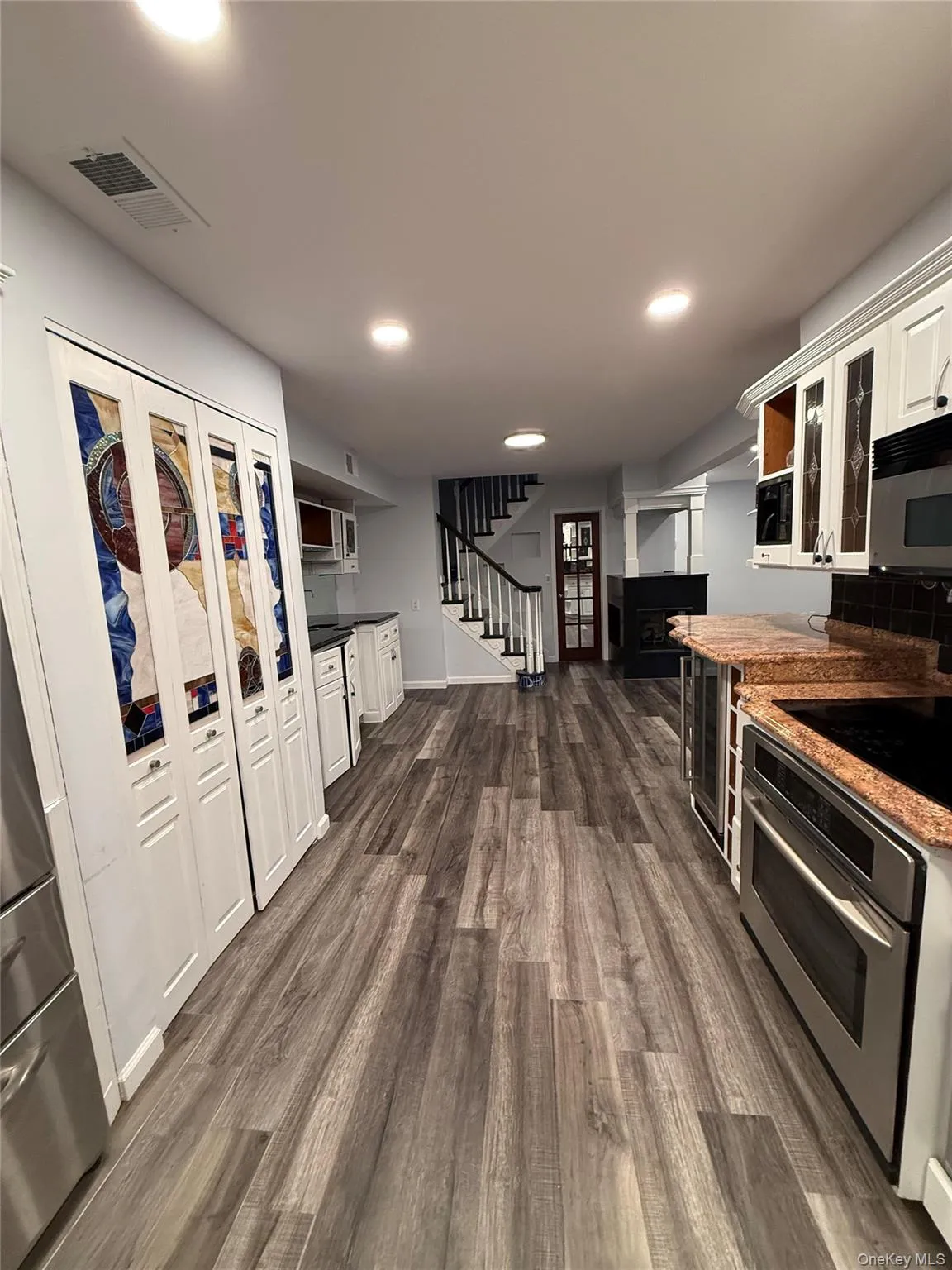 Kitchen with white cabinetry, glass insert cabinets, dark wood-style floors, stainless steel appliances, and dark stone countertops Kitchen with white cabinetry, glass insert cabinets, dark wood-style floors, stainless steel appliances, and dark stone countertops