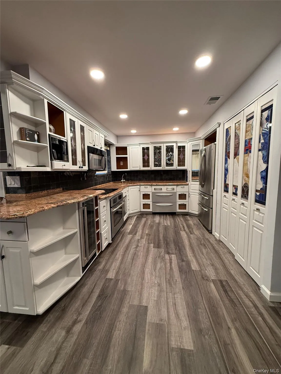 Kitchen featuring open shelves, white cabinetry, dark wood-type flooring, glass insert cabinets, and stainless steel appliances Kitchen featuring open shelves, white cabinetry, dark wood-type flooring, glass insert cabinets, and stainless steel appliances