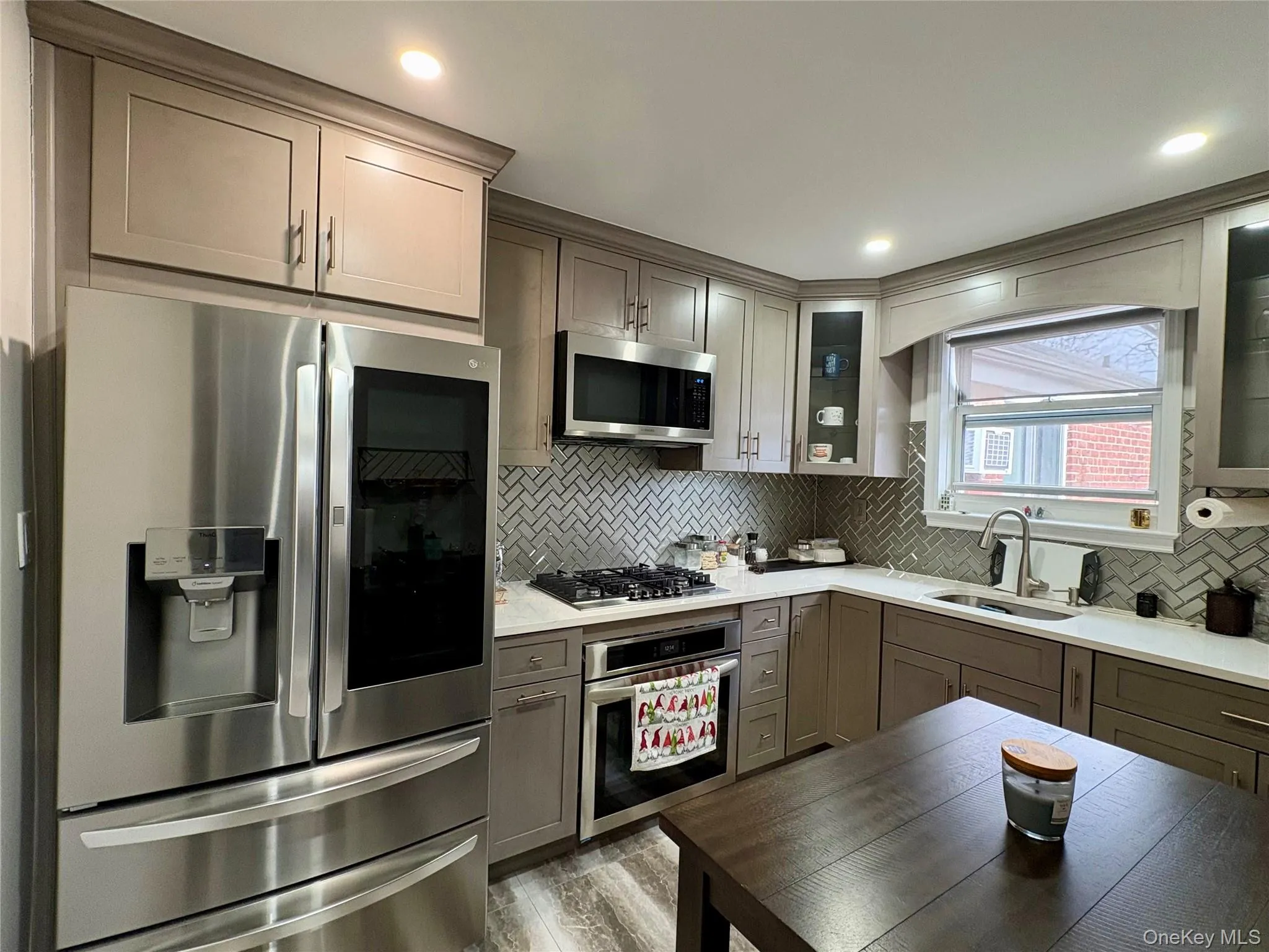 Kitchen with appliances with stainless steel finishes, light stone counters, backsplash, gray cabinets, and recessed lighting Kitchen with appliances with stainless steel finishes, light stone counters, backsplash, gray cabinets, and recessed lighting