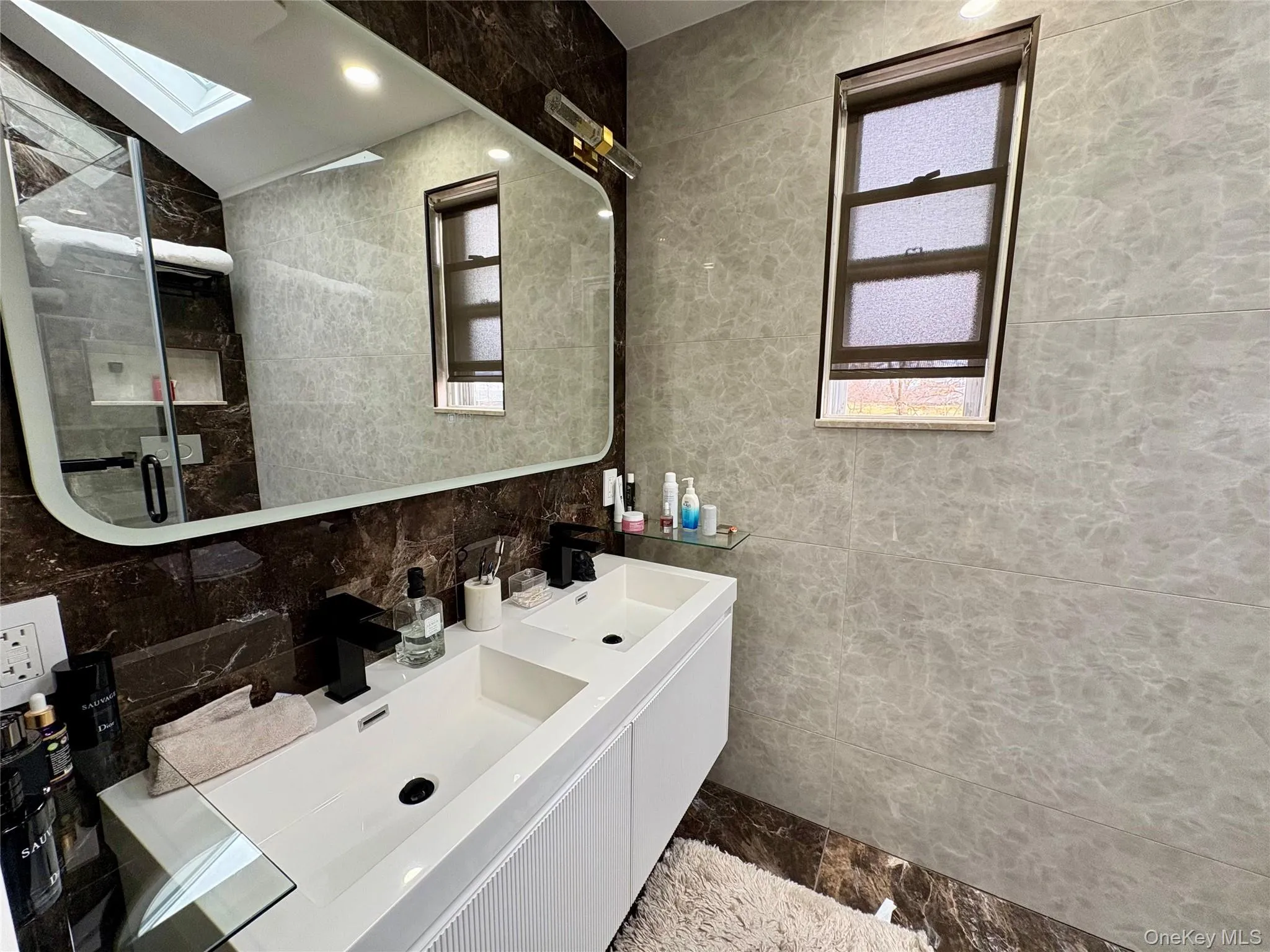 Bathroom featuring double vanity, a skylight, tile walls, and a shower stall Bathroom featuring double vanity, a skylight, tile walls, and a shower stall
