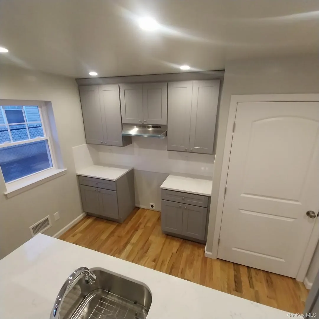 Kitchen with gray cabinetry, light wood-style floors, under cabinet range hood, recessed lighting, and light stone countertops Kitchen with gray cabinetry, light wood-style floors, under cabinet range hood, recessed lighting, and light stone countertops